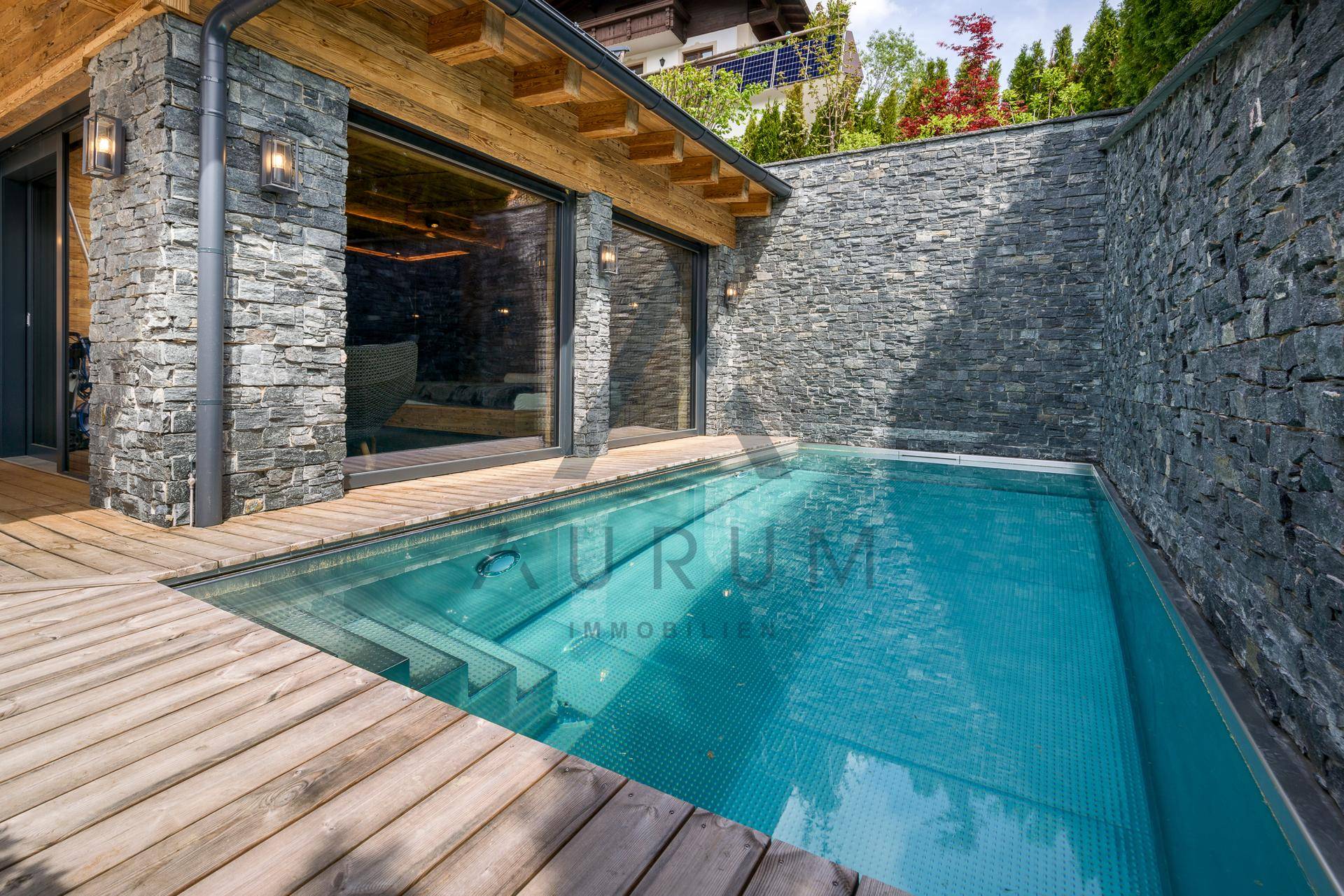 Kleiner, erfrischender Pool auf der Holzterrasse, umgeben von Natursteinmauern und dem Gebäude.