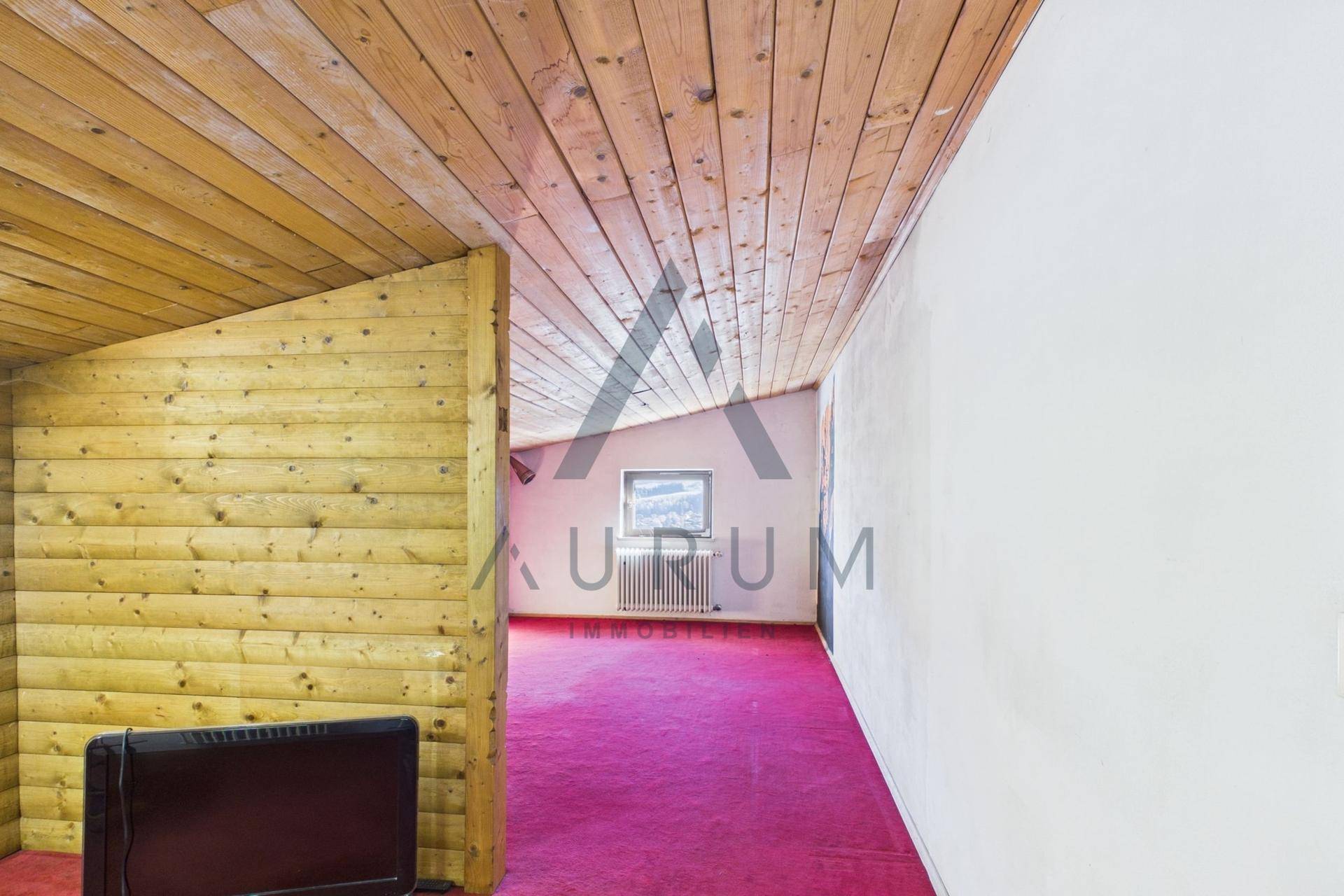 Dachgeschossraum mit Holzverkleidung, schrägen Decken und Teppichboden.