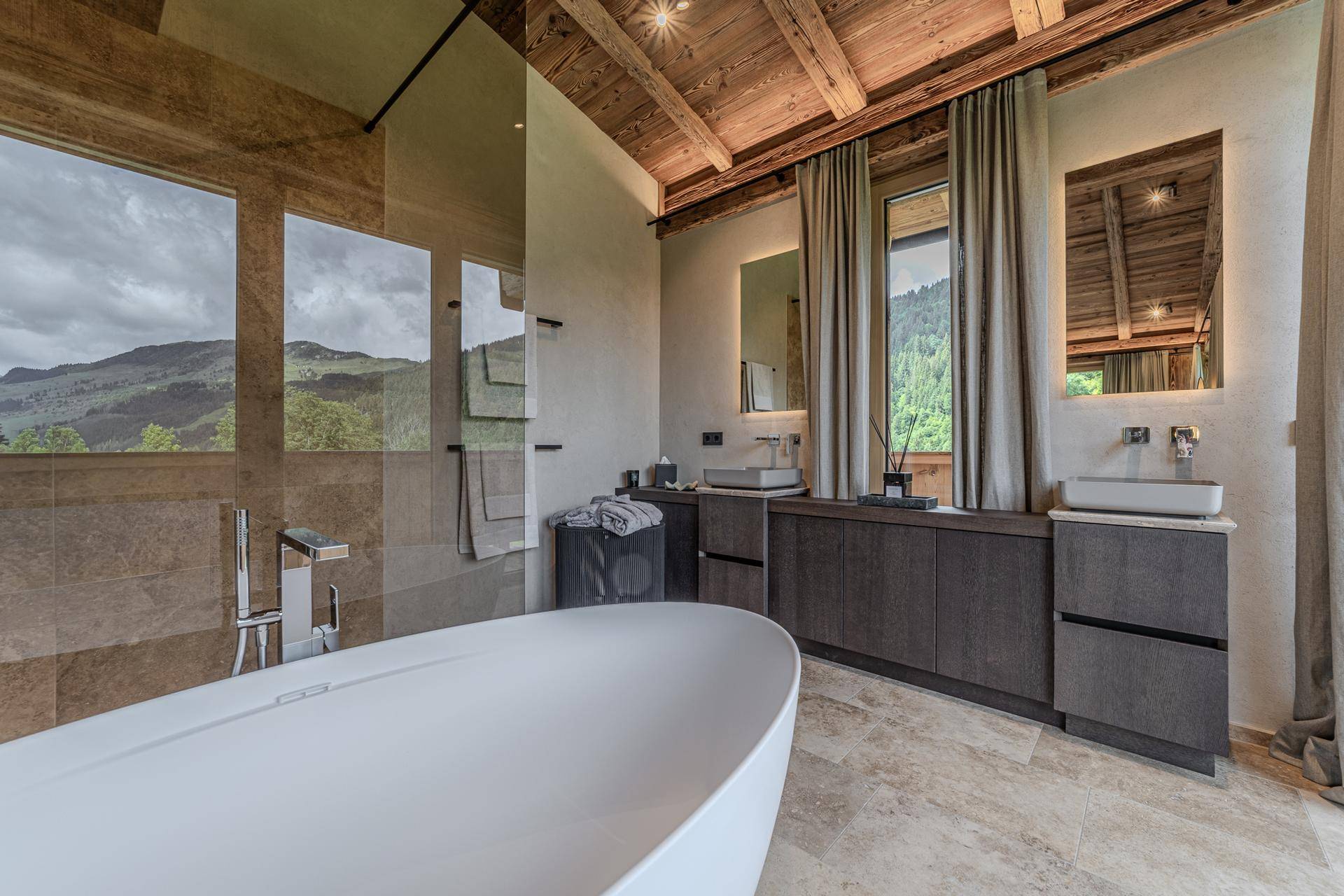 Modernes Badezimmer mit freistehender Badewanne, Doppelwaschbecken und Bergblick durch große Fenster.