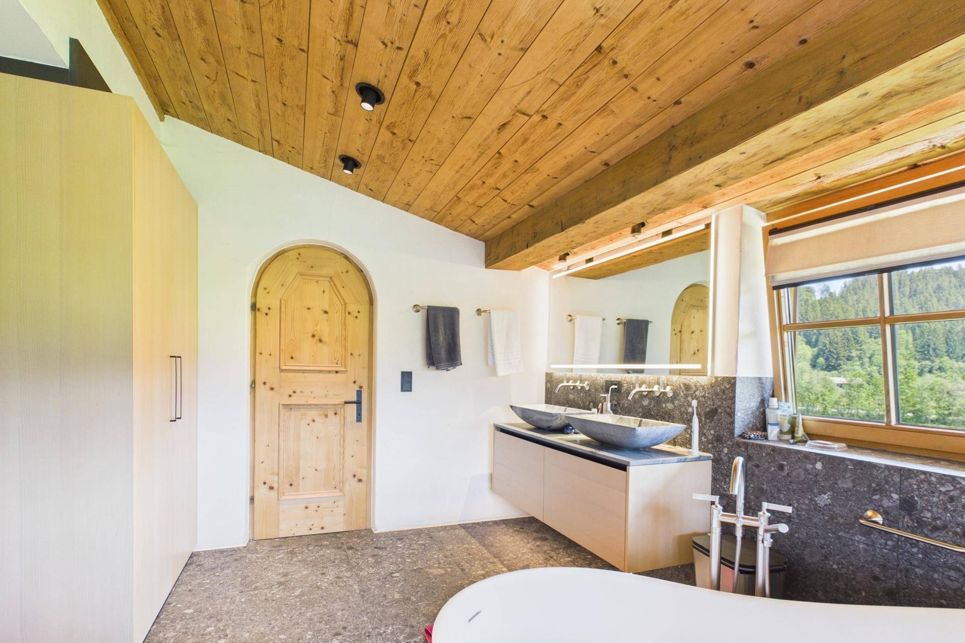 Elegantes Badezimmer mit Holzbalkendecke, Doppelwaschbecken und Holztür.
