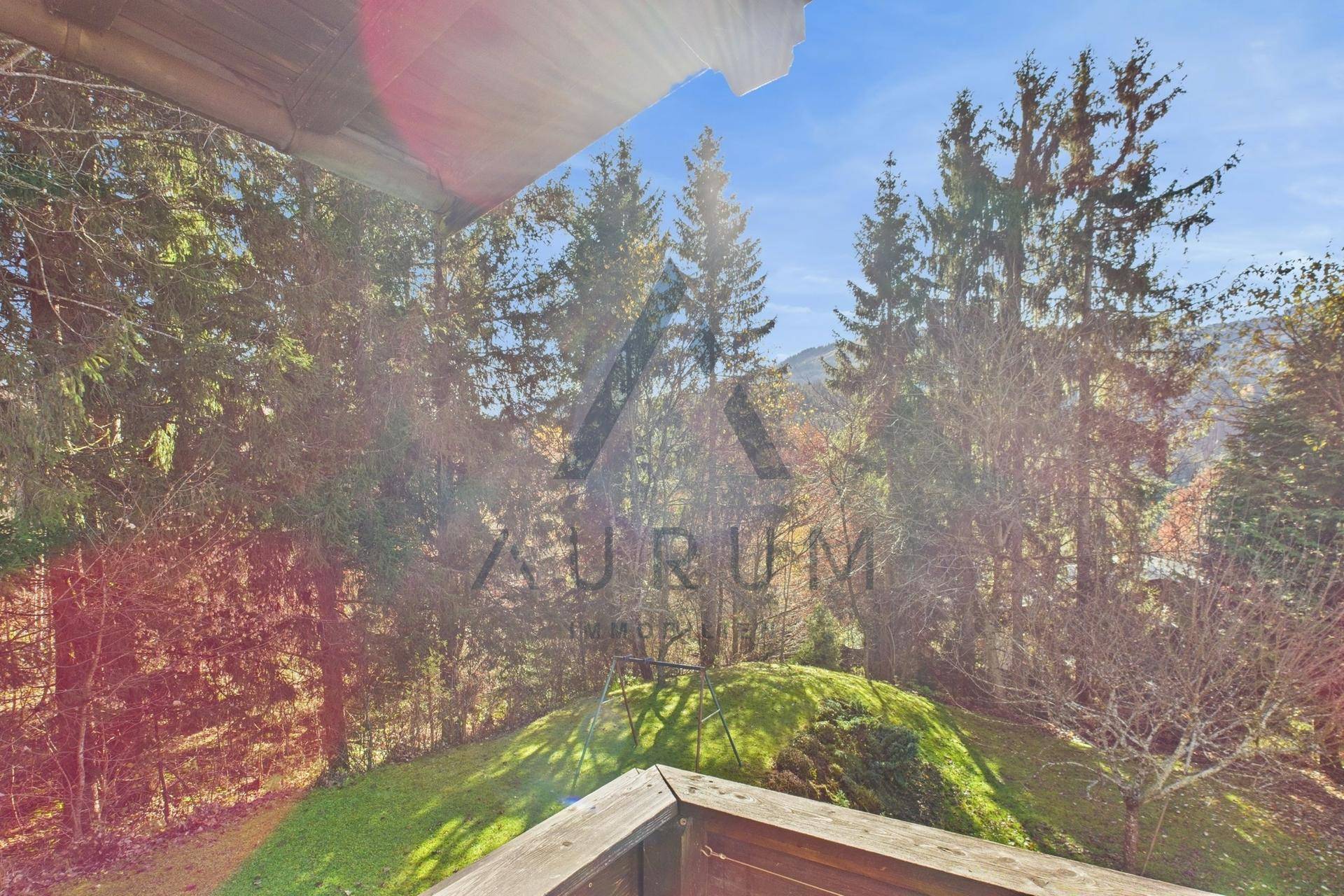 Balkon mit Holzboden und Geländer, umgeben von Bäumen und Blick ins Grüne.