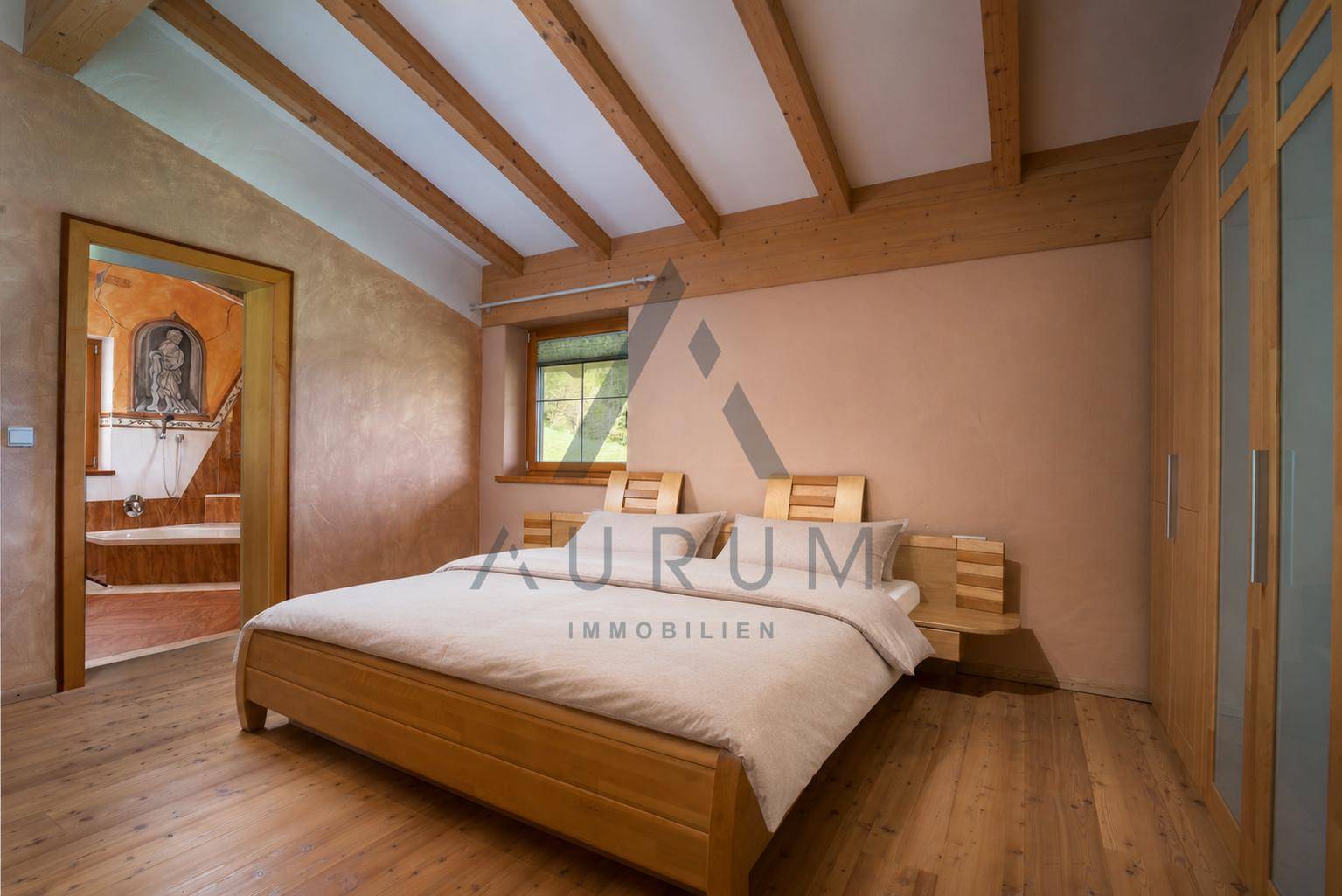 Schlafzimmer mit Holzboden, sichtbaren Deckenbalken und einem Fenster, das einen Blick auf die Landschaft bietet.