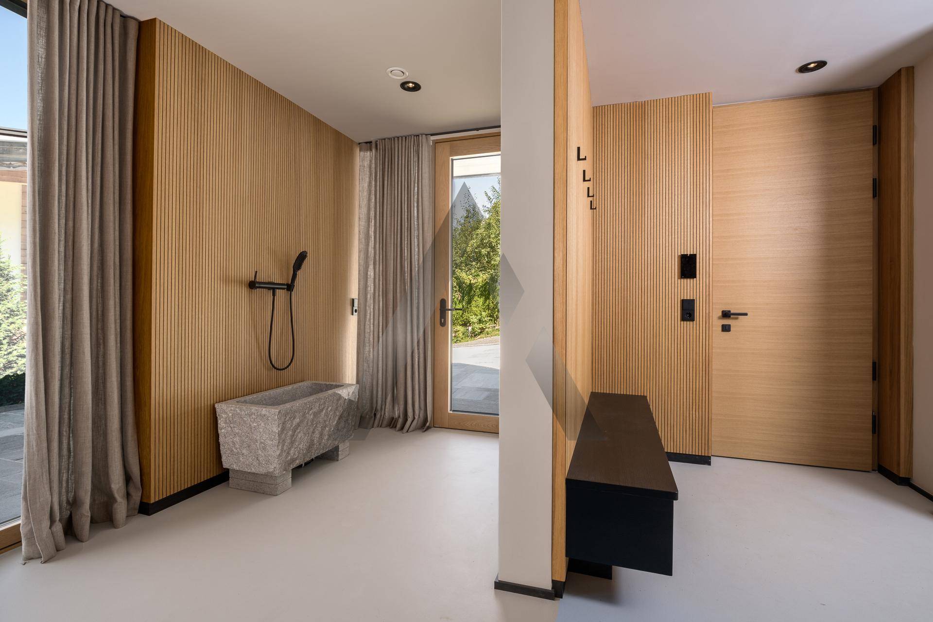 Heller Eingangsbereich mit Holzverkleidung, Steintrog und Zugang zum Außenbereich.