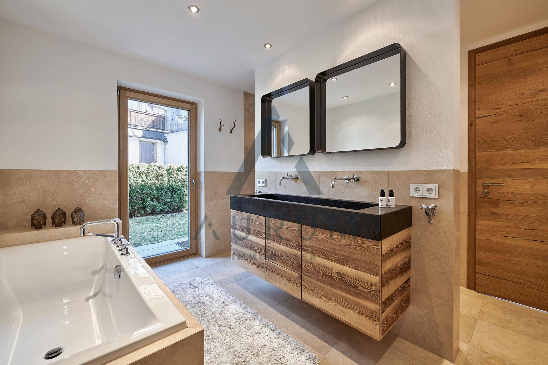 Großes Badezimmer mit Badewanne, Doppelwaschbecken und Fenster, bietet Zugang zum Außenbereich.