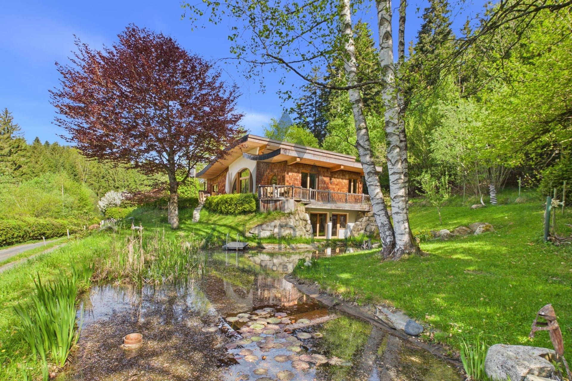Weitläufiges Anwesen mit Holzhaus, großem Teich und altem Baumbestand in ländlicher Lage.