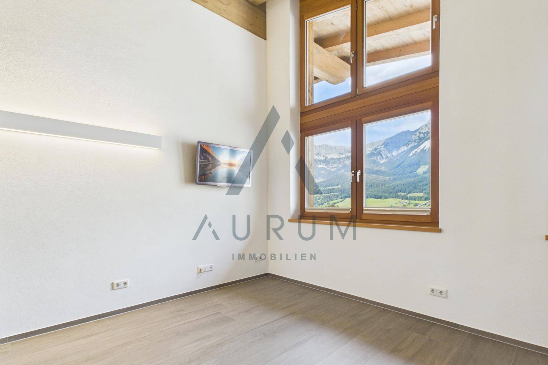 Heller Raum mit großen Fenstern, Bergblick und sichtbaren Holzdeckenbalken im Dachgeschoss.