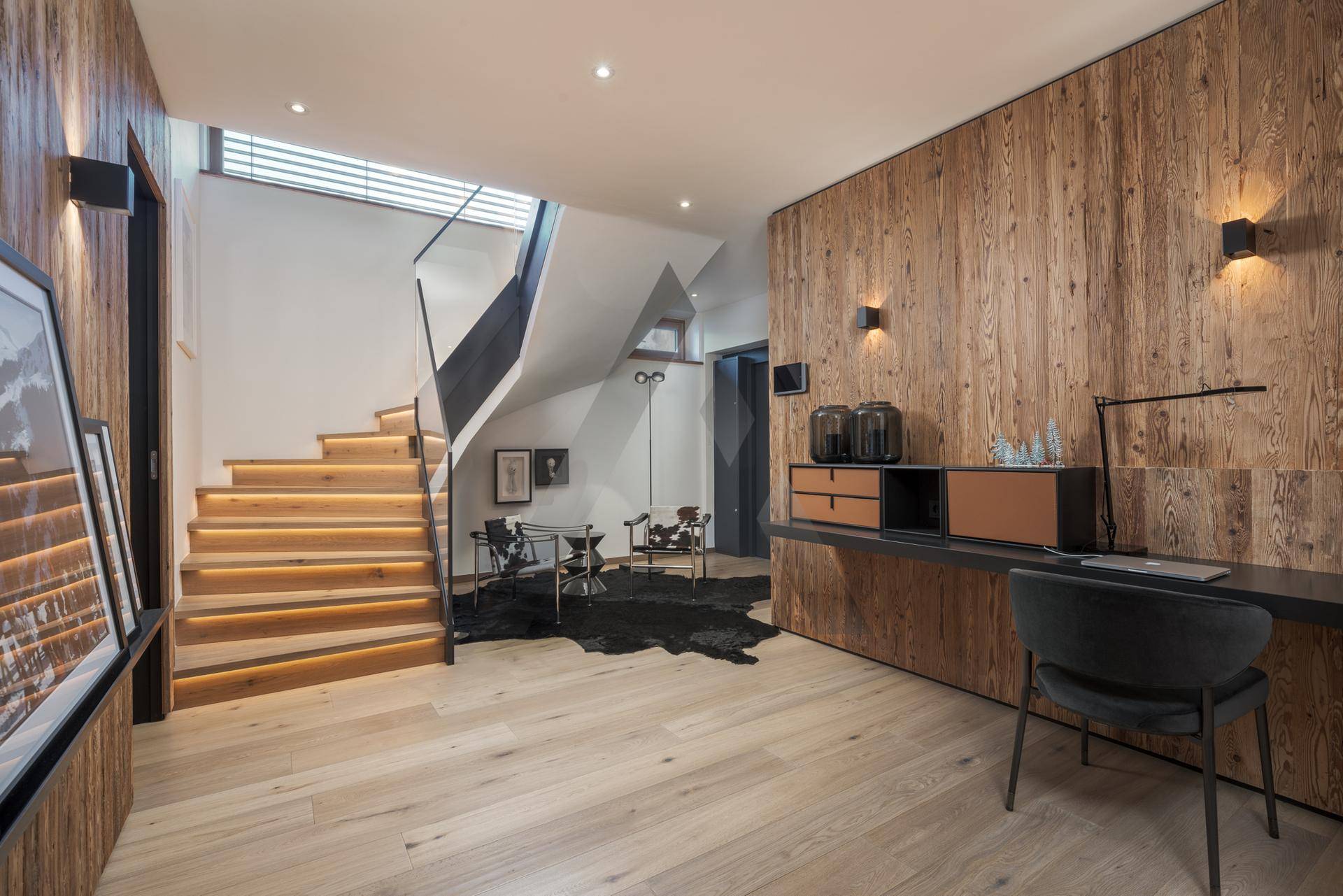 Geräumiger Flur mit beleuchteter Holztreppe, Holzwand und integriertem Arbeitsbereich.