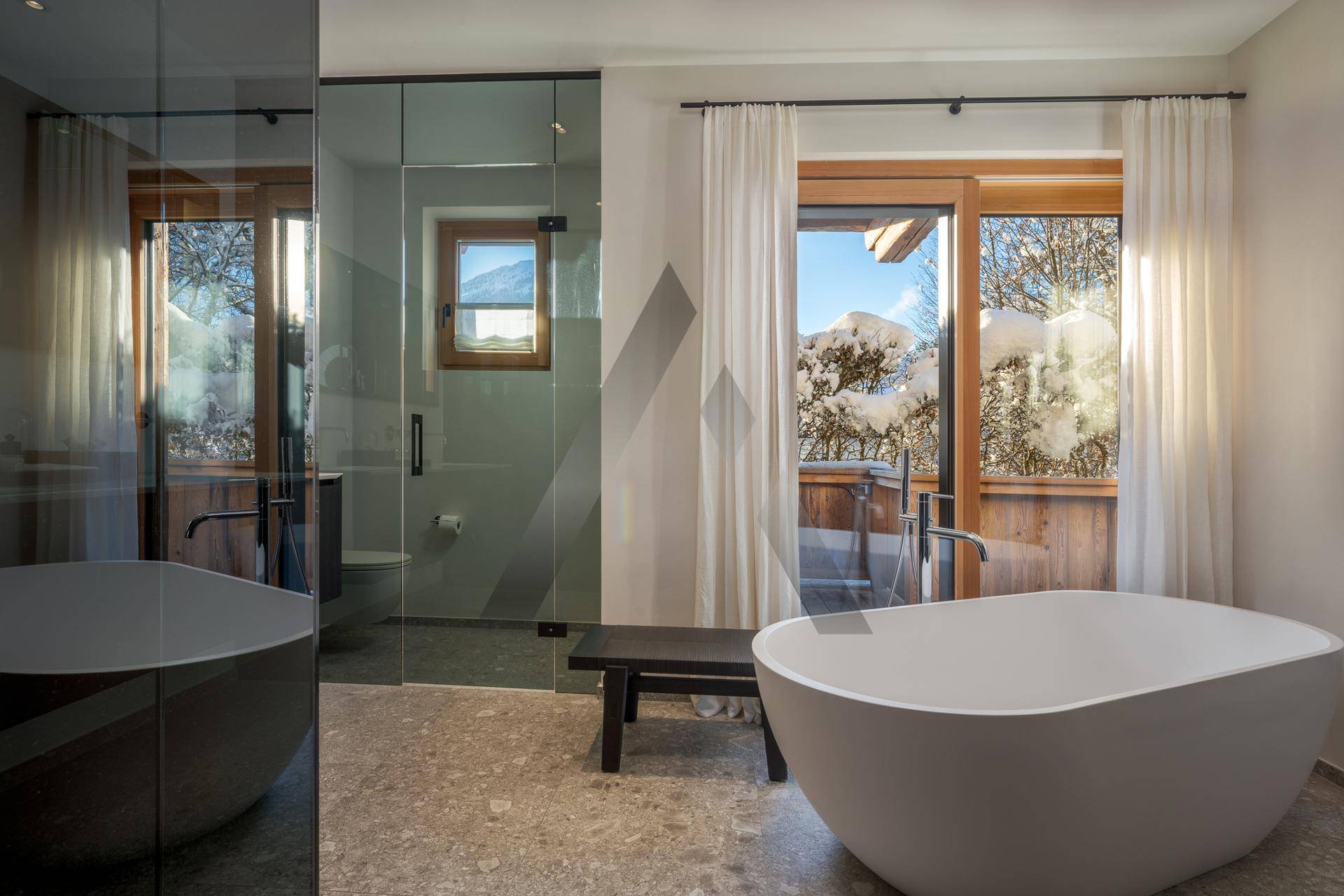 Elegantes Badezimmer mit freistehender Badewanne, Dusche und Balkonzugang mit Bergblick.