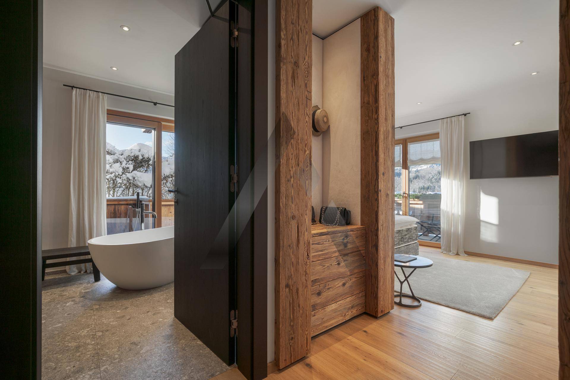 Geräumiges Schlafzimmer mit freistehender Badewanne, Holzelementen und Balkonzugang mit Bergblick.