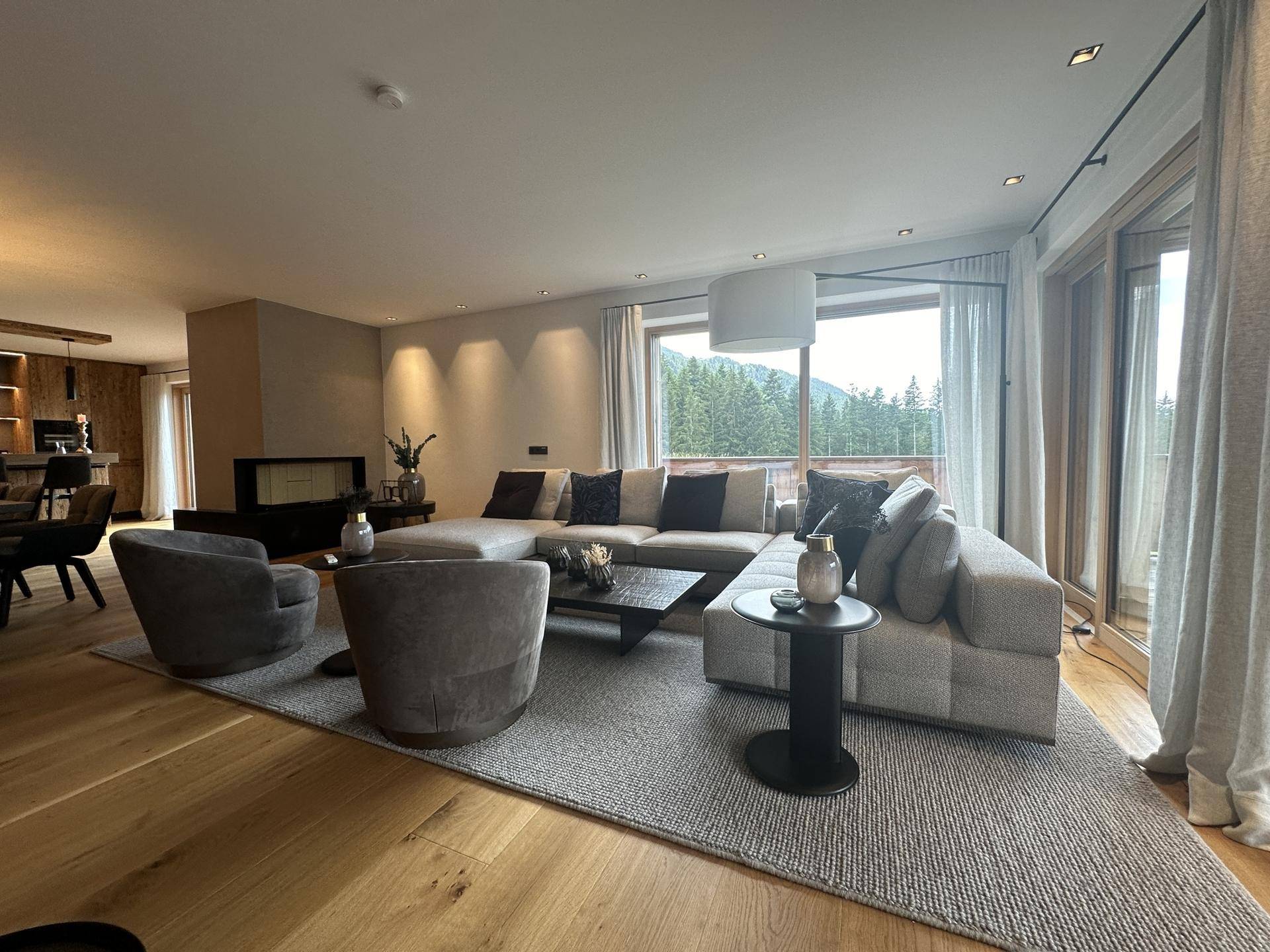 Gemütliches Wohnzimmer mit großem Sofa, Kamin und weitem Blick auf die grüne Natur.