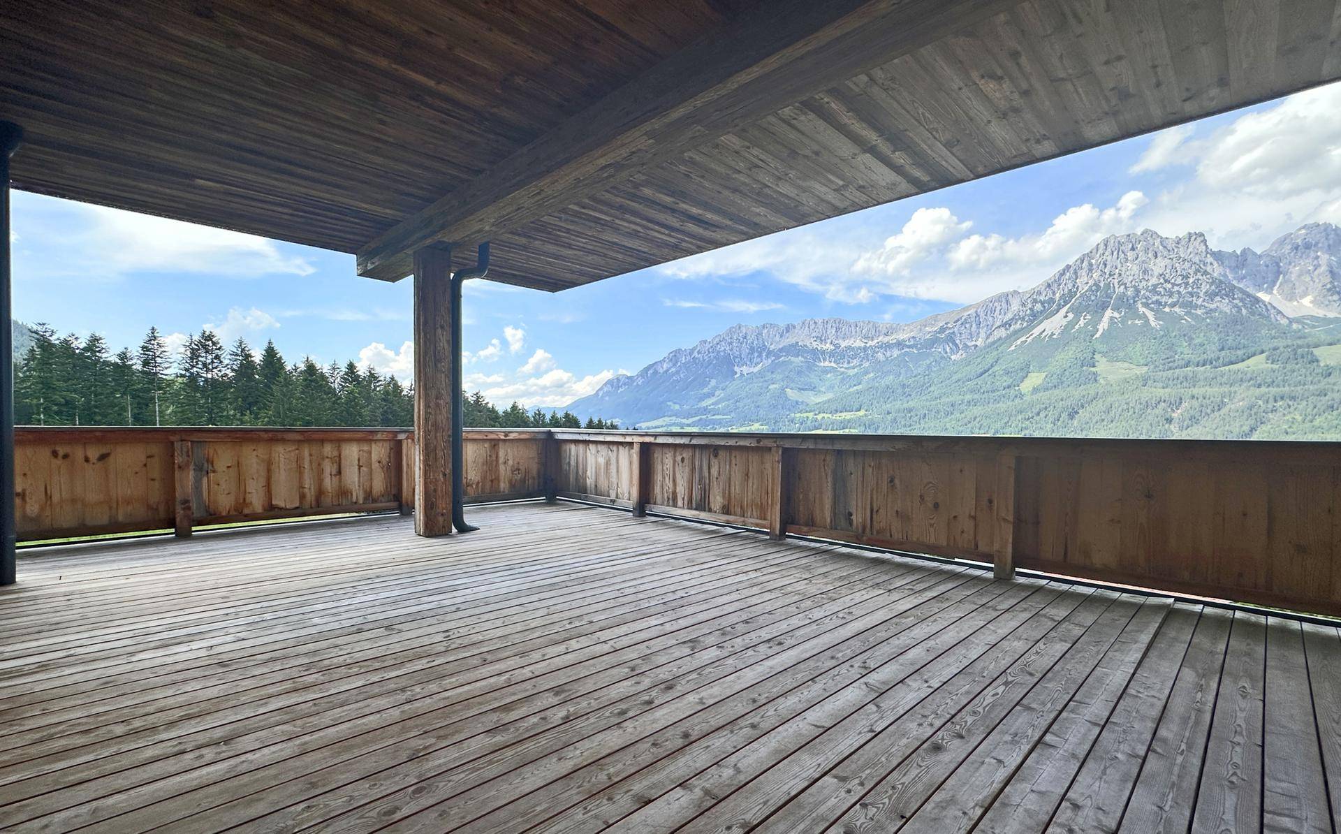 Geräumige überdachte Holzterrasse mit beeindruckendem Blick auf die umliegenden Berge.