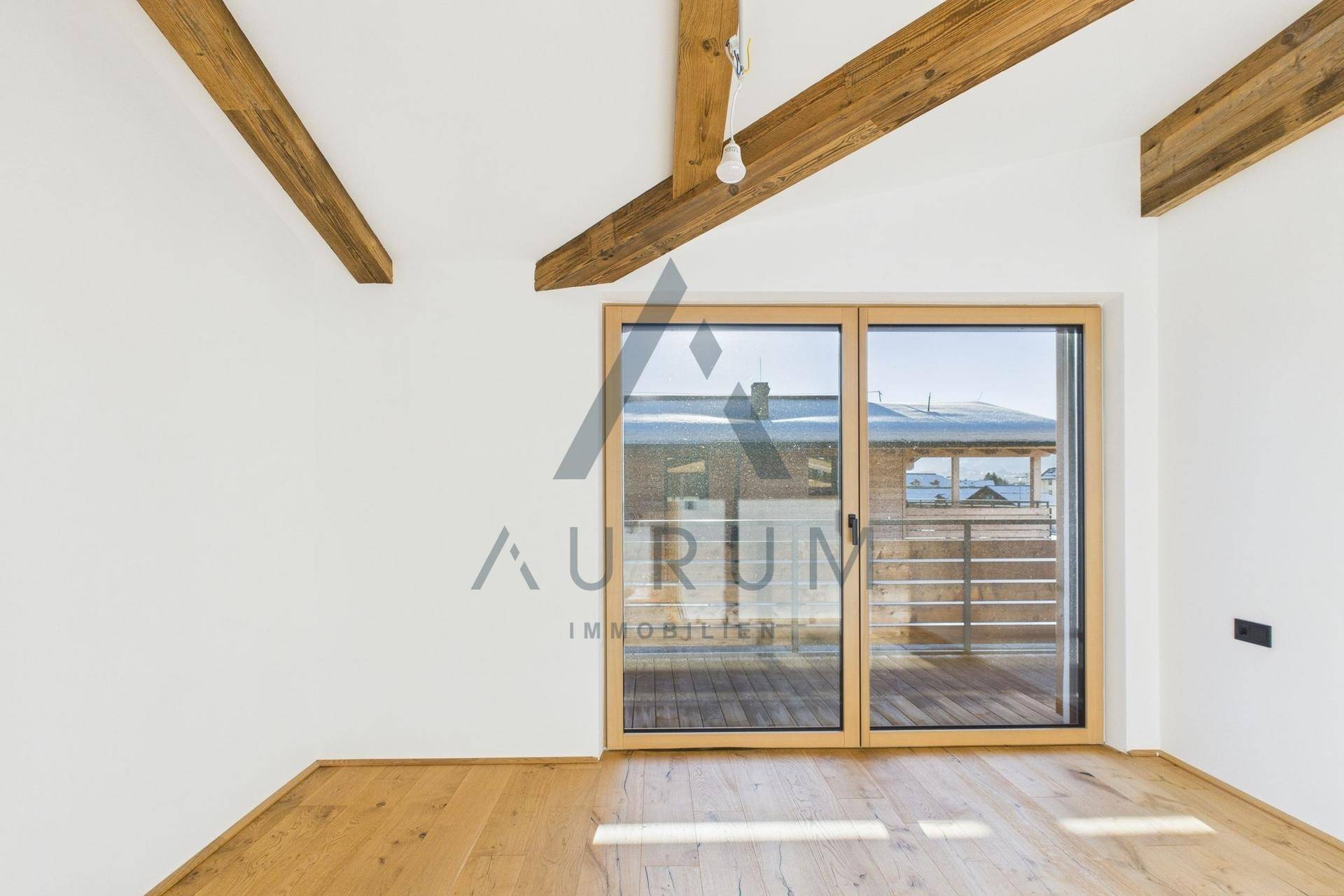 Heller Innenraum mit Holzboden und großer Schiebetür, die auf einen Balkon mit Bergblick führt.