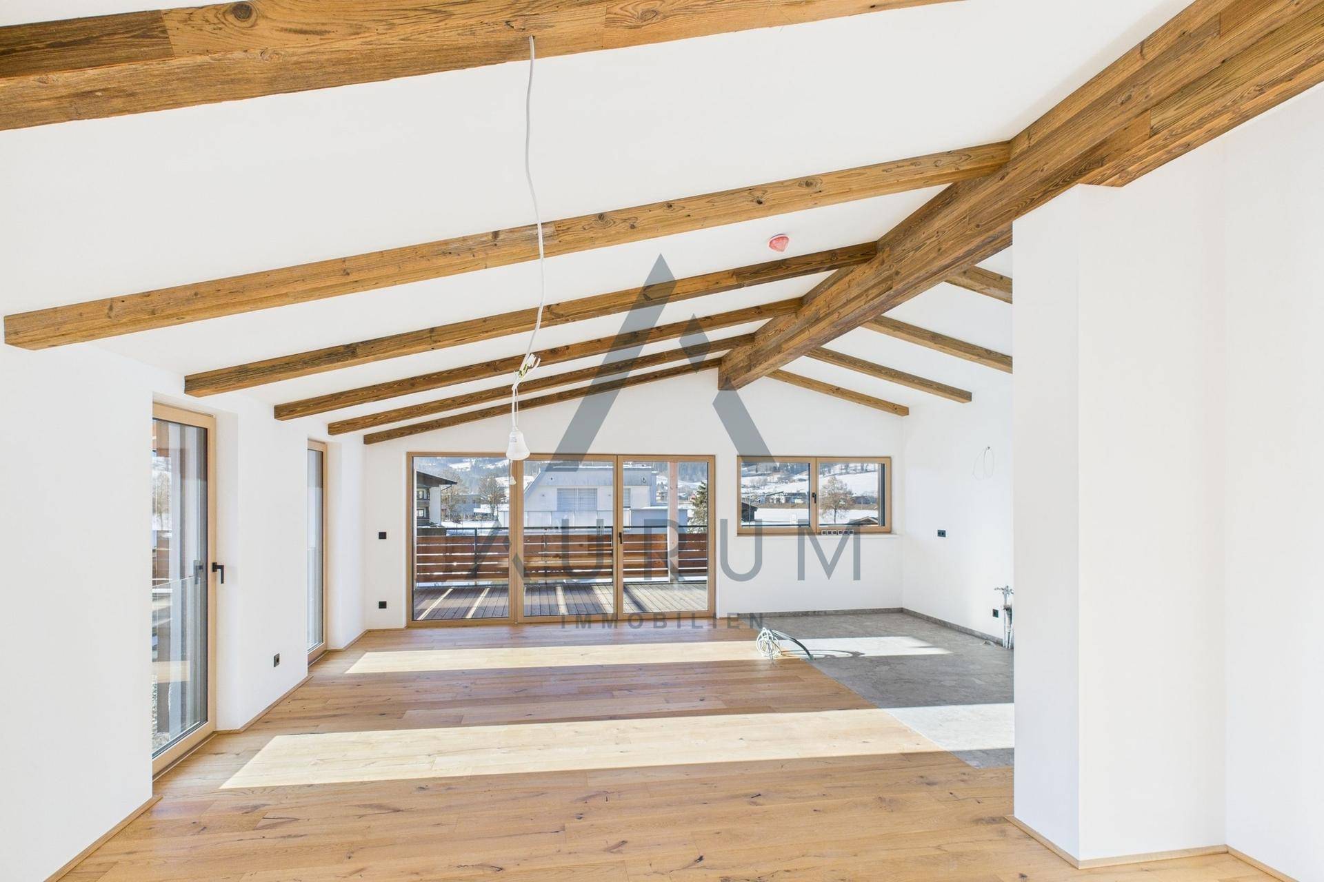 Großer, heller Raum mit sichtbaren Holzbalken, Holzboden und Zugang zu einem Balkon mit Bergblick.