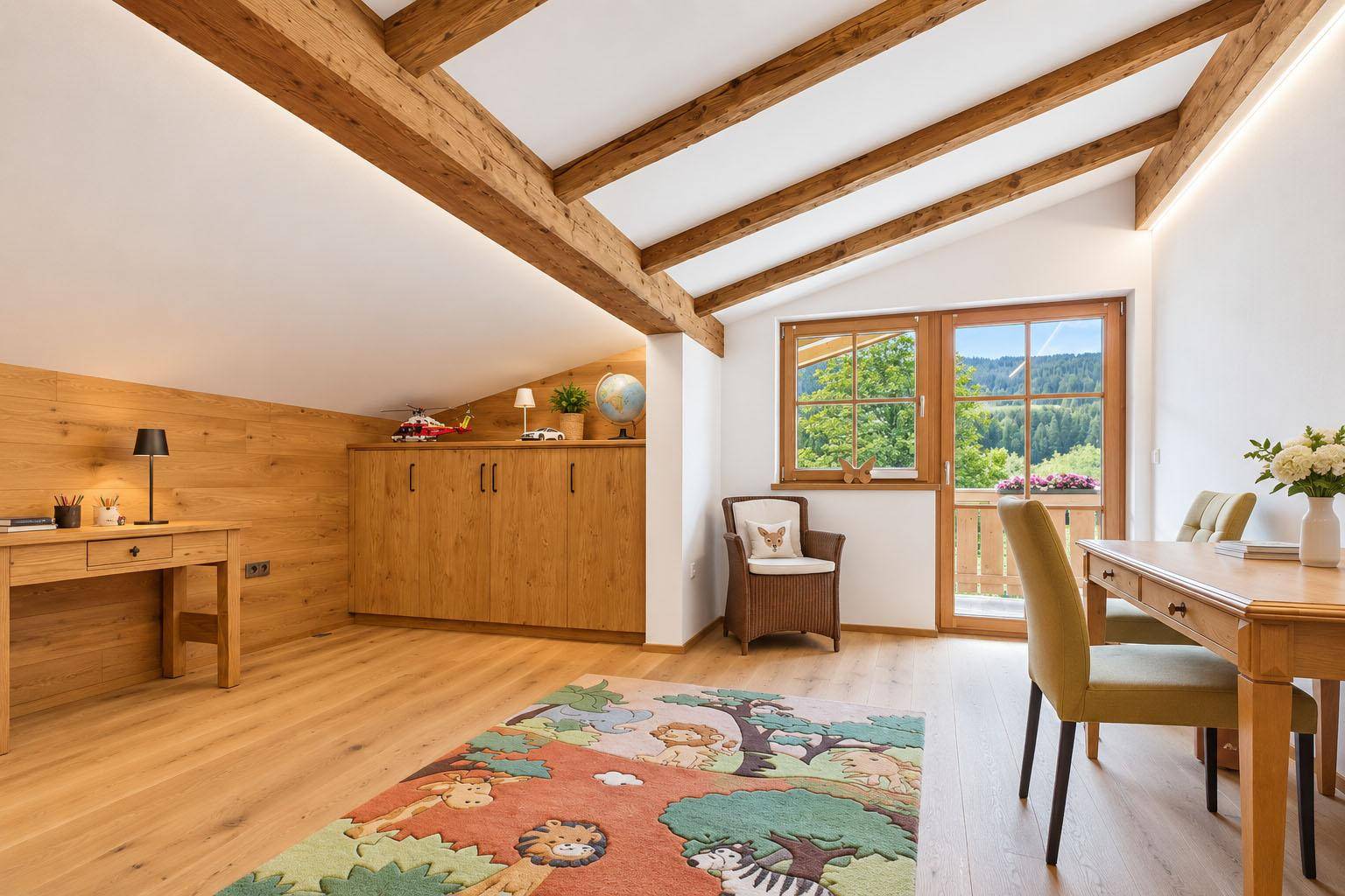 Helles Dachzimmer mit Holzbalken, Schreibtisch und Zugang zu einem kleinen Balkon.