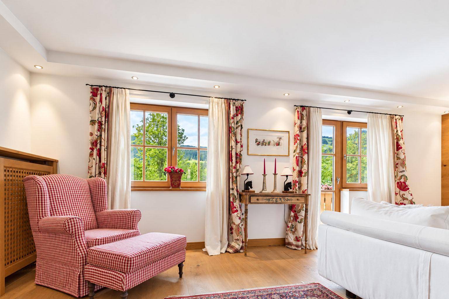 Gemütlicher Wohnbereich mit Sessel, Holzboden und großen Fenstern mit Blick auf die Natur.