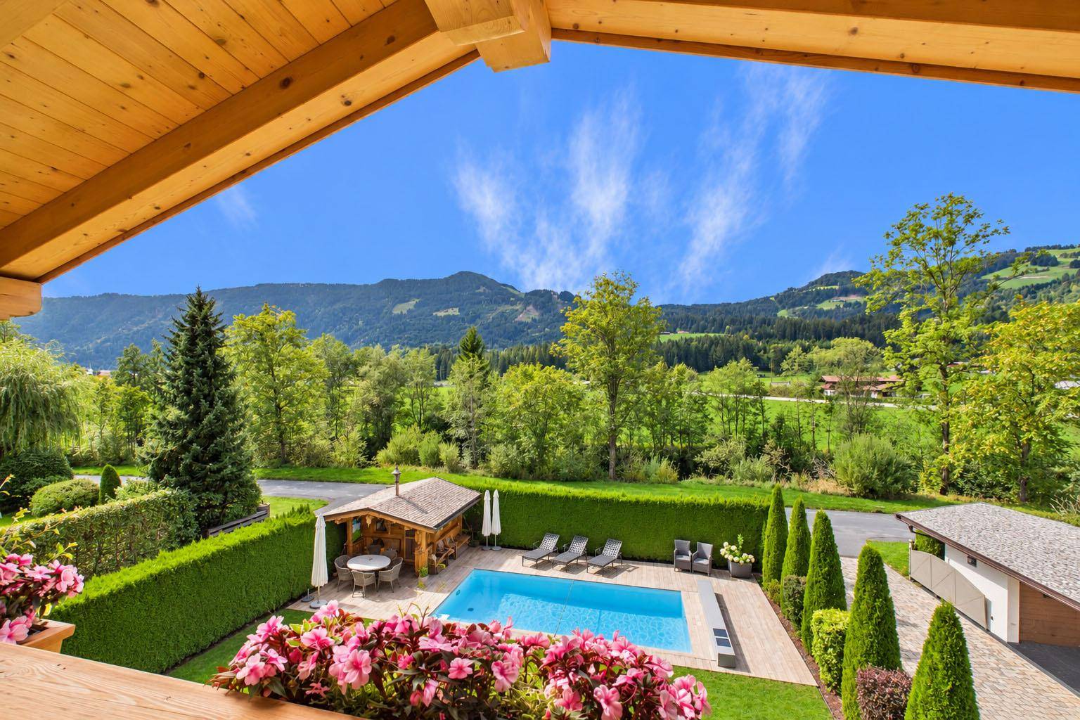 Panoramablick vom Balkon auf den gepflegten Garten mit Pool und die umliegende Berglandschaft.