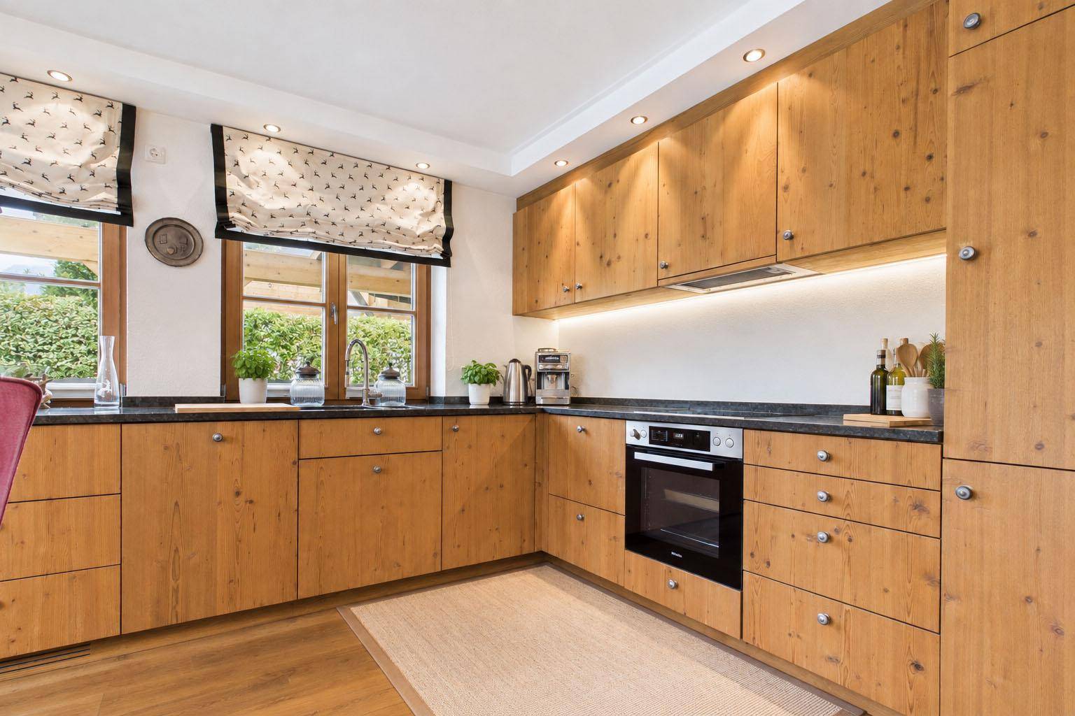 Detailansicht der Holzküche mit modernen Einbaugeräten und Arbeitsplatte aus dunklem Stein.