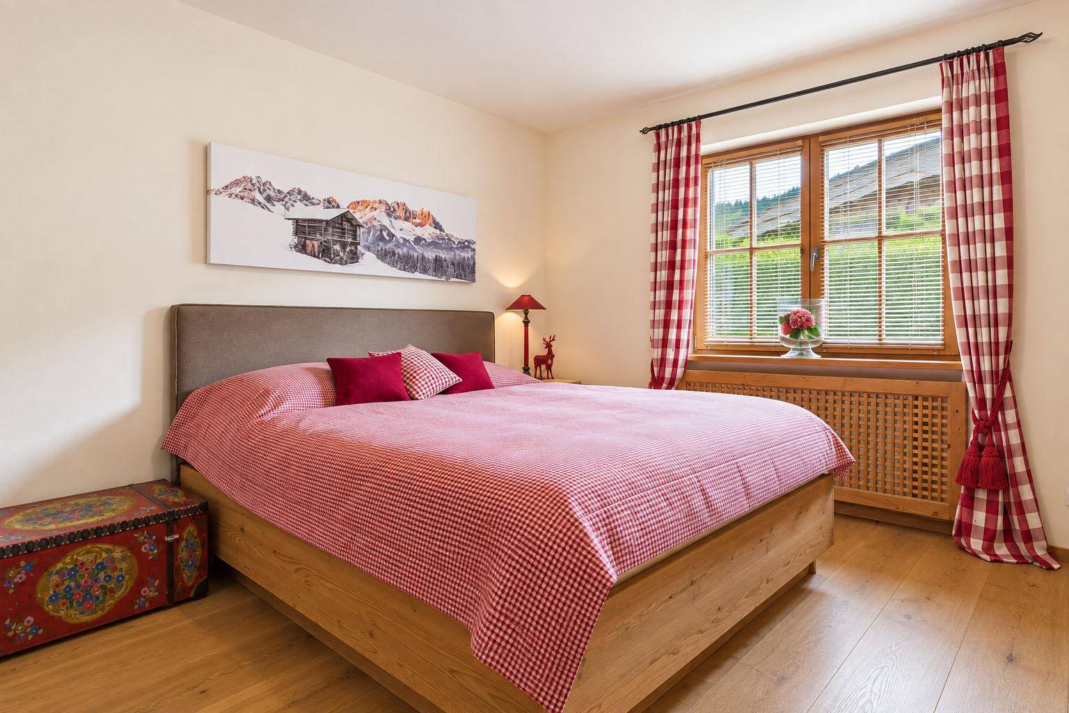 Schlafzimmer im Landhausstil mit Holzfußboden, karierter Bettwäsche und Blick ins Grüne.