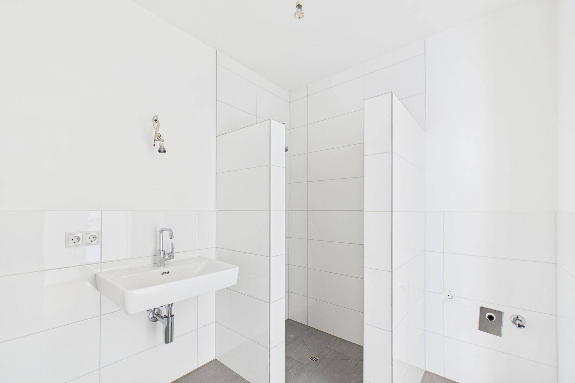 Helles Badezimmer mit Waschbecken und vorbereitetem Bereich für eine begehbare Dusche.