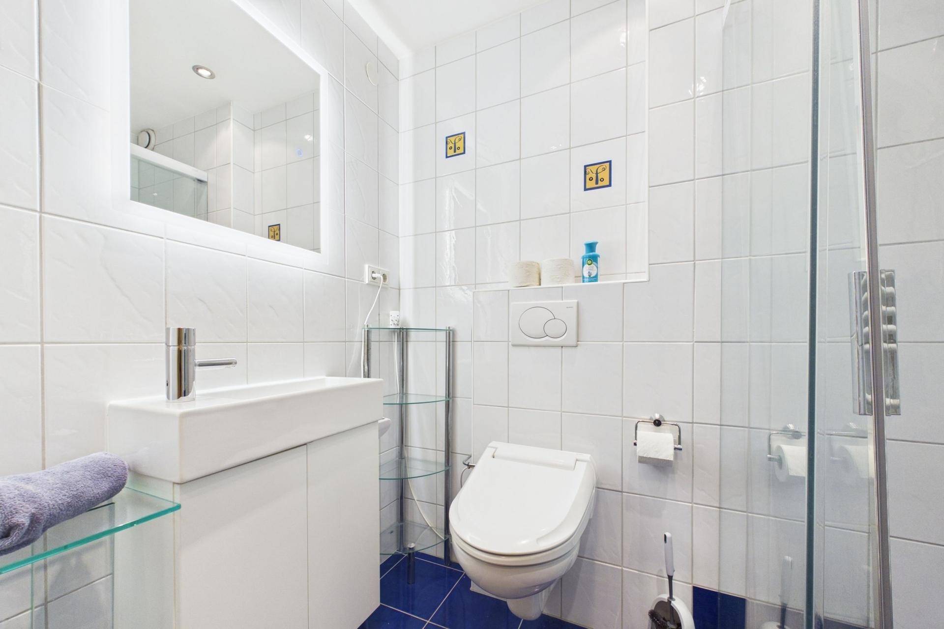 Modernes Badezimmer mit Waschtisch, WC, Duschbereich und Spiegel mit Beleuchtung.