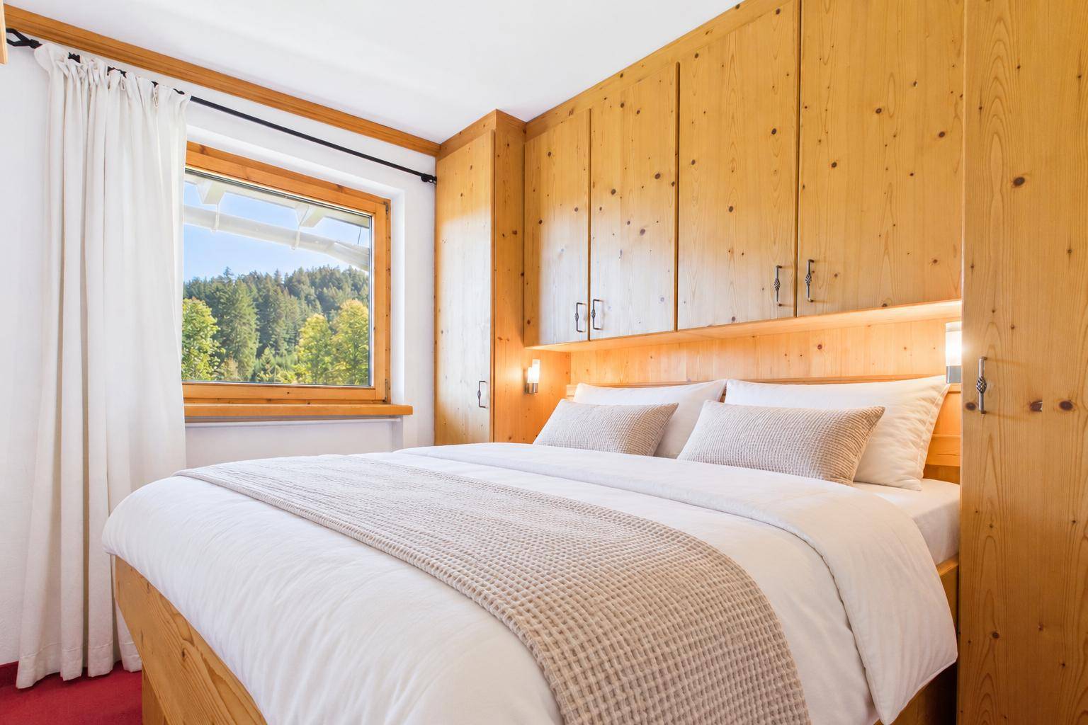 Gemütliches Schlafzimmer mit Holzeinbauten, Doppelbett und Fenster mit Blick ins Grüne.