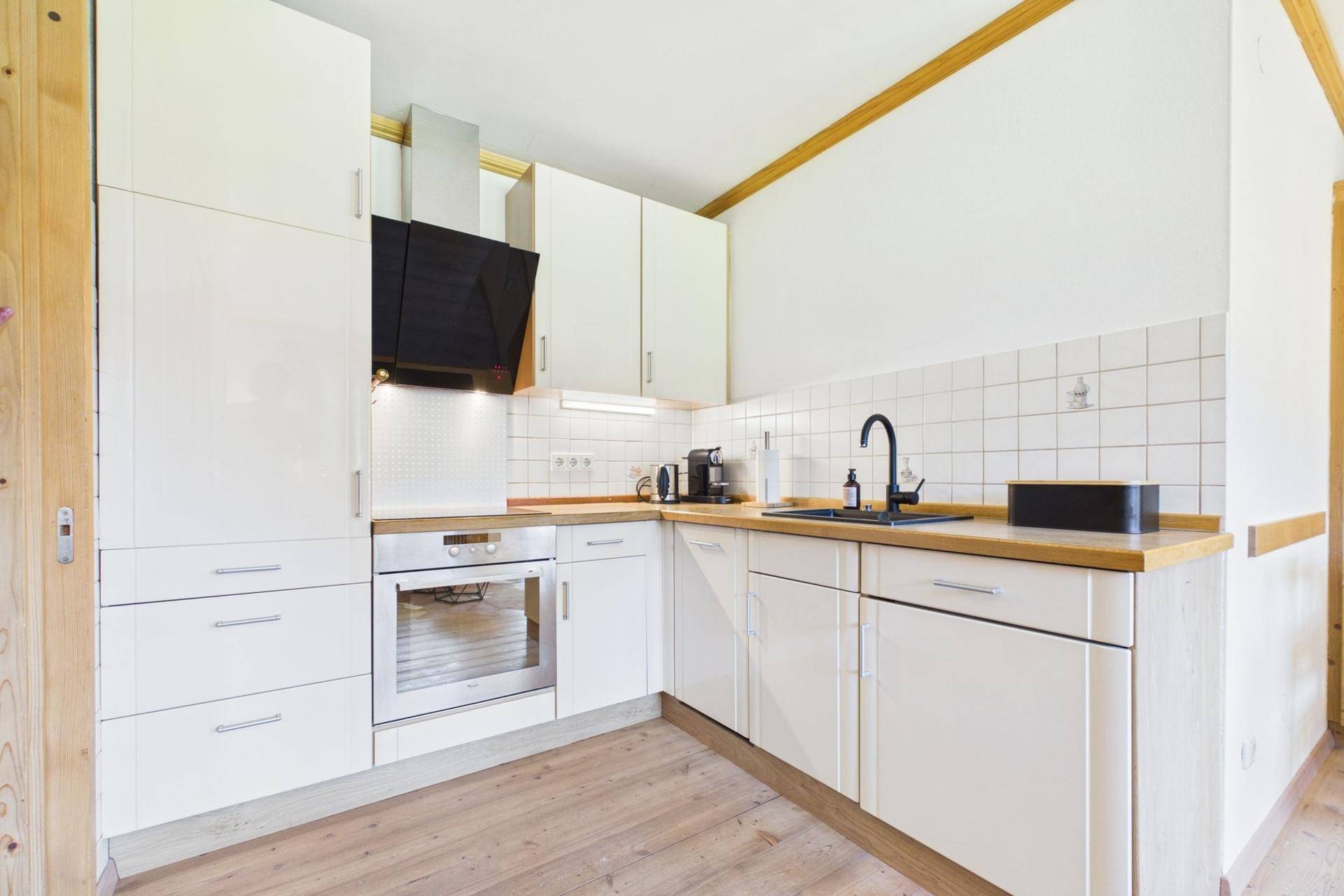 Moderne weiße Küche mit Holzarbeitsplatte, integriertem Backofen und Dunstabzugshaube in hellem Ambiente.