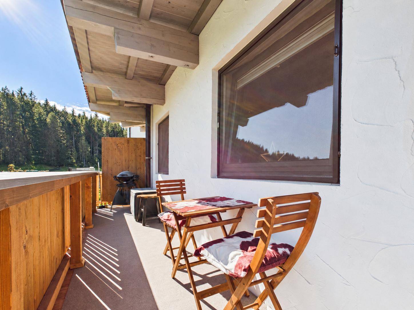 Sonniger Balkon mit Holzboden, Sitzgelegenheiten und Grill für entspannte Stunden im Freien.