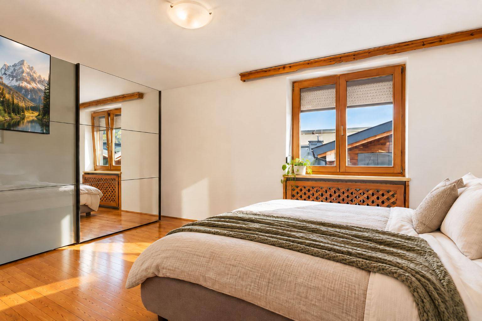 Schlafzimmer mit großem Spiegelschrank, Holzboden und Fenster mit Blick auf die Dächer.