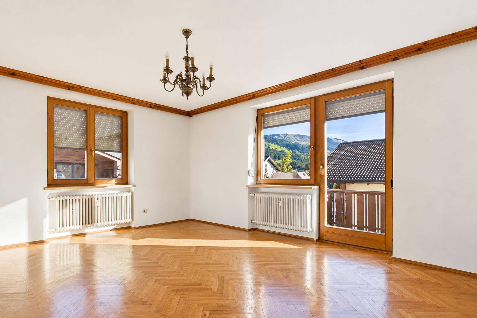 Helles Wohnzimmer mit Fischgrätparkett, traditionellem Kronleuchter und Zugang zum Balkon.