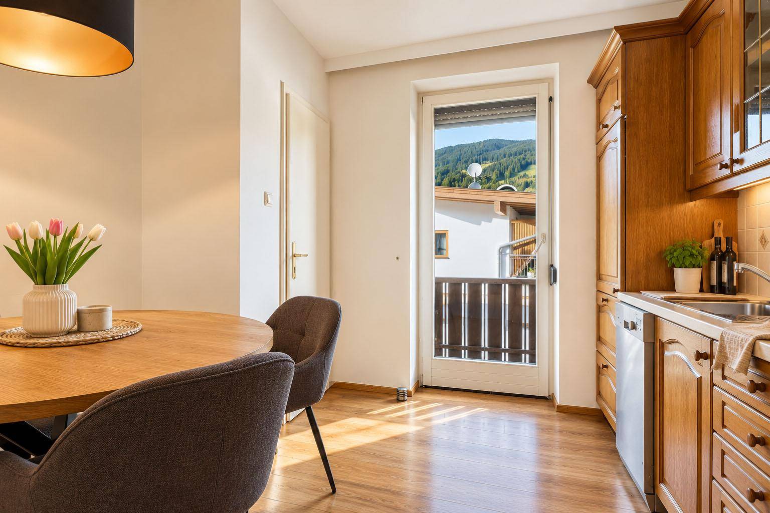 Essbereich in der Küche mit Holztisch, modernen Stühlen und Blick auf die grüne Berglandschaft.