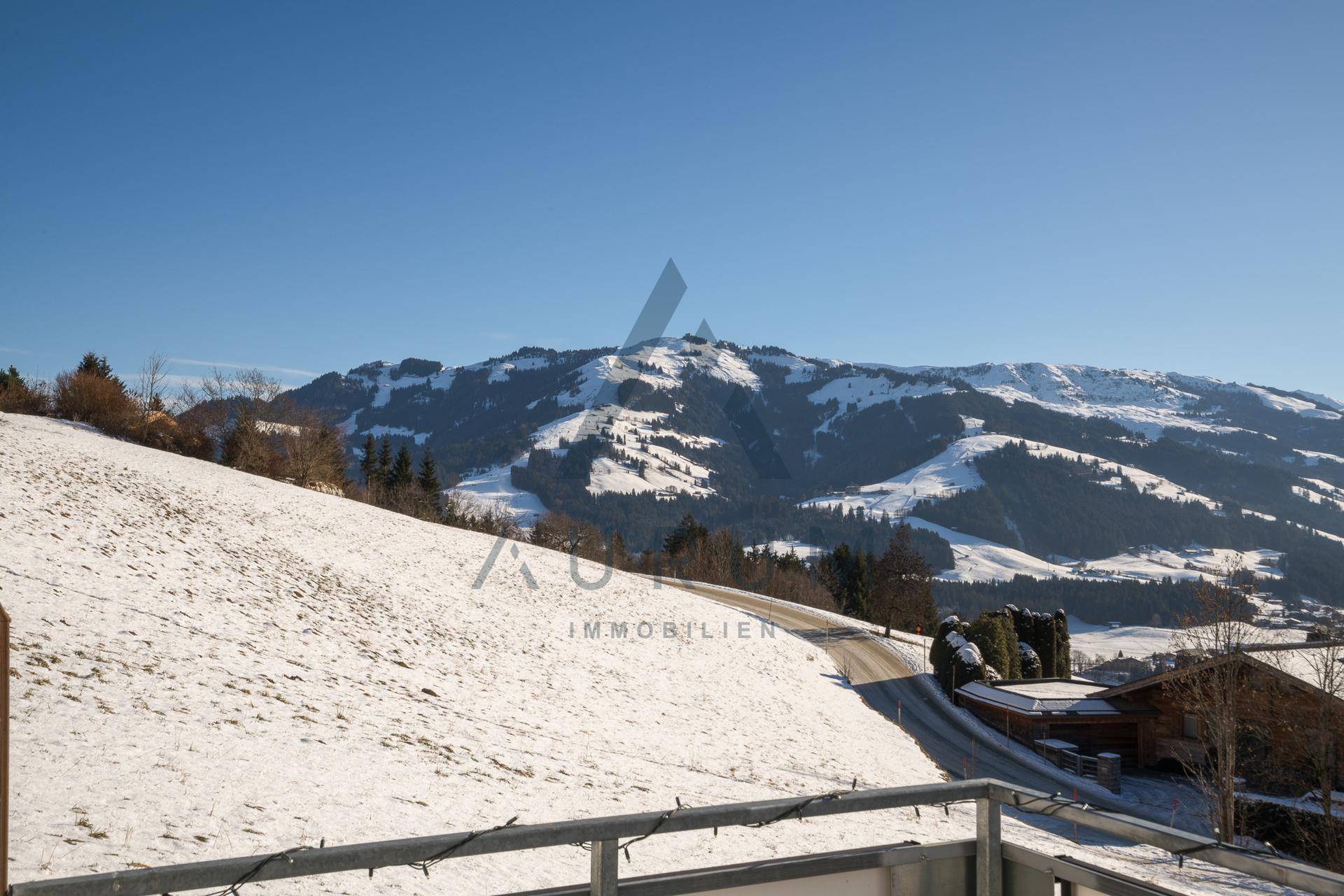 Panoramablick von einem Balkon auf eine verschneite Hügellandschaft mit Häusern und Bergen.