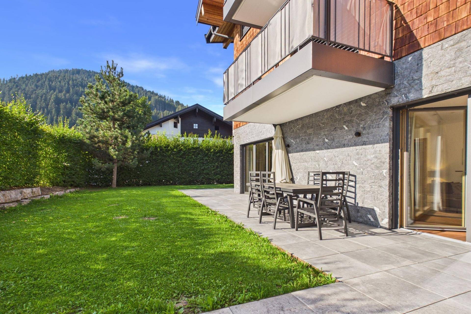 Gepflegter Garten mit Rasenfläche und einer möblierten Terrasse neben dem modernen Gebäude.