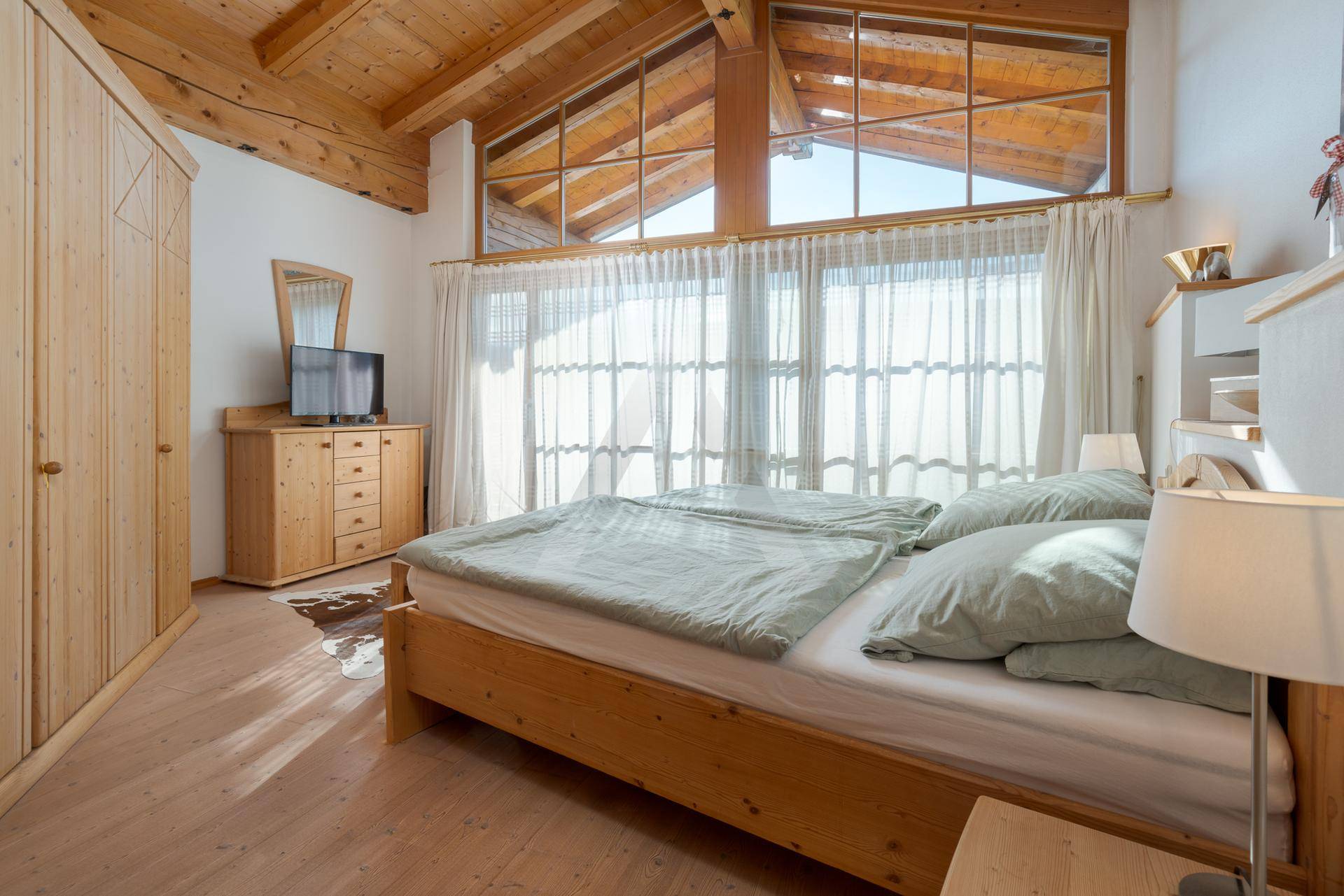 Geräumiges Schlafzimmer mit Holzbalkendecke, Einbauschränken und großen Fenstern.