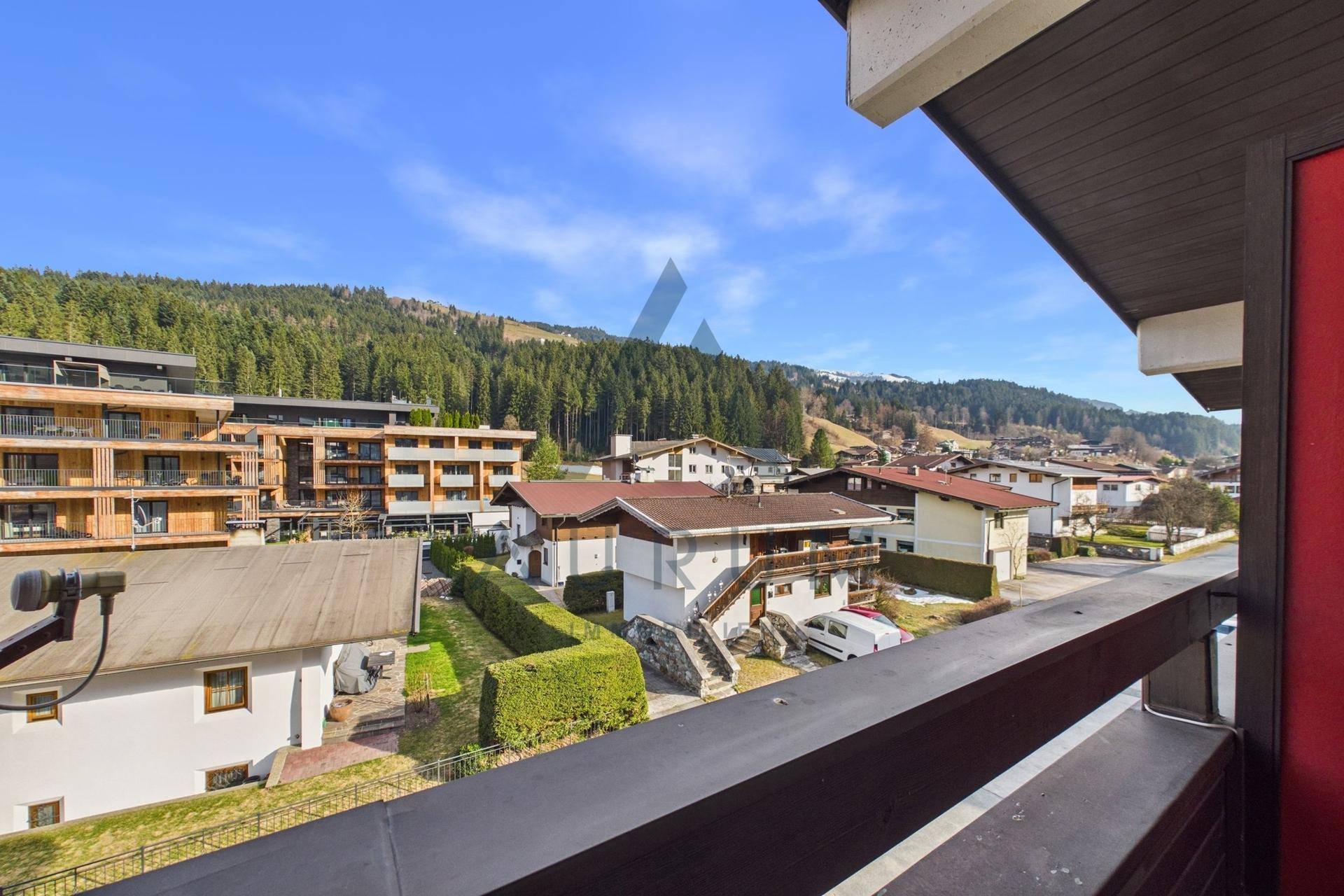 Blick vom Balkon auf die umliegende Wohnbebauung und die bewaldeten Hügel.