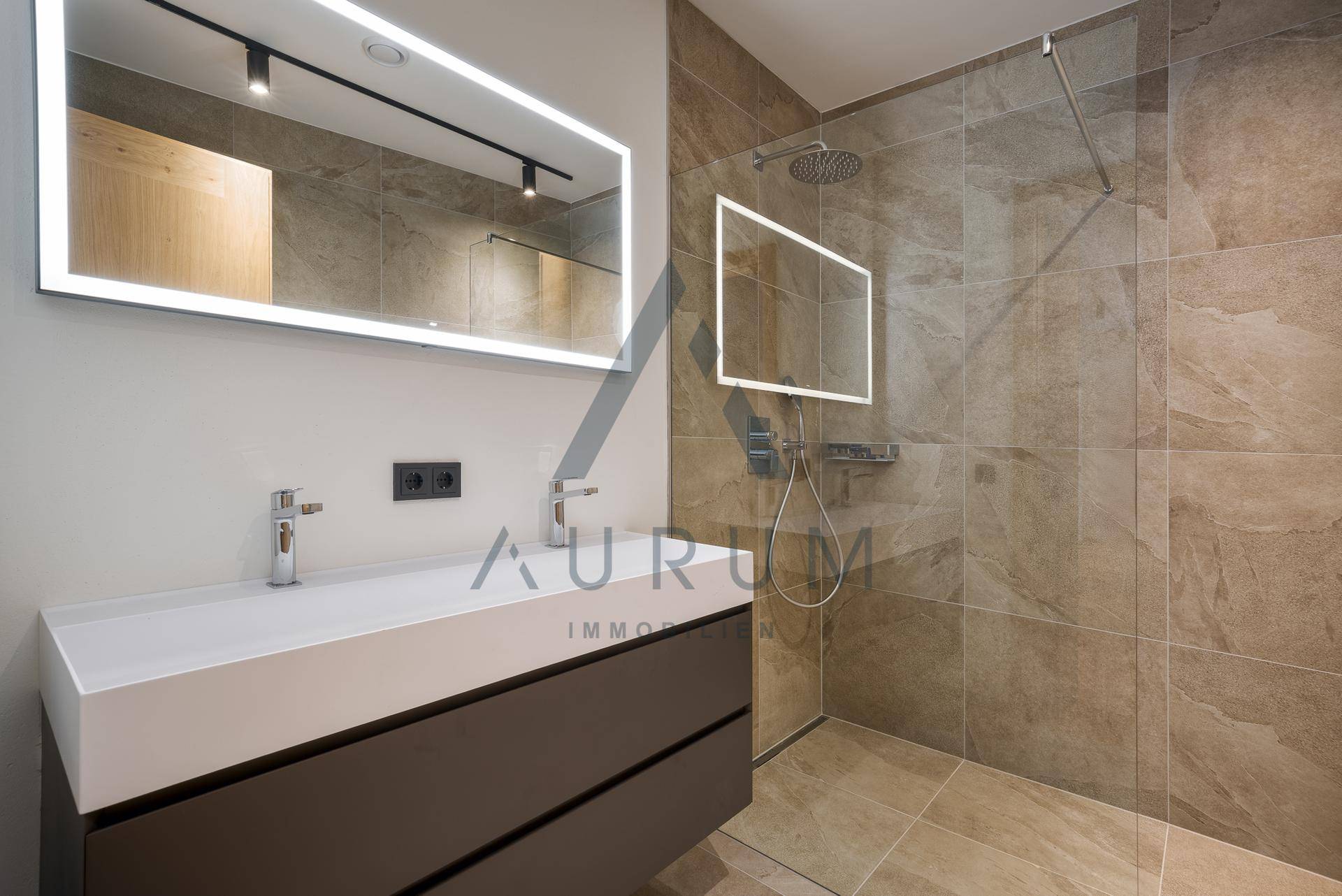 Modernes Badezimmer mit großformatigen Fliesen, beleuchtetem Spiegel und ebenerdiger Dusche.