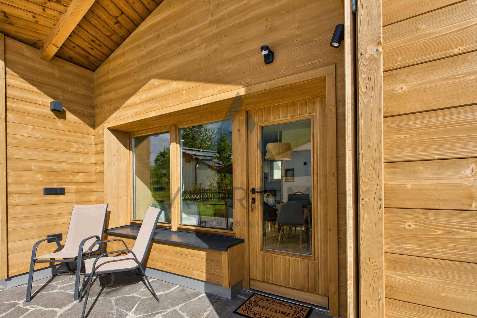Eingangsbereich mit kleiner Terrasse und Sitzgelegenheiten am modernen Holzhaus.