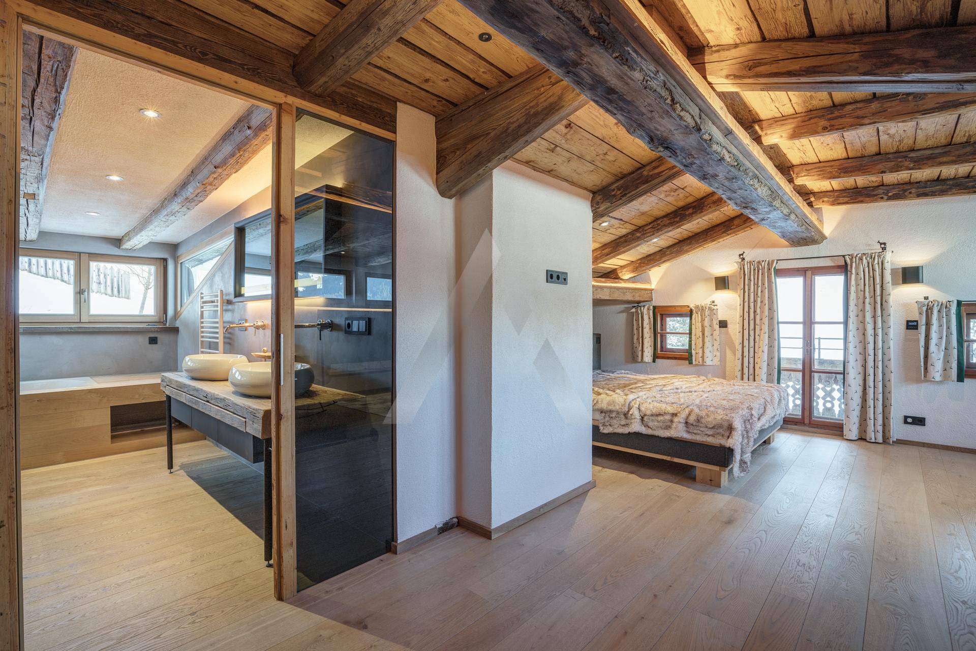Offenes Schlafzimmer mit Holzbalken und integriertem Badezimmerbereich.