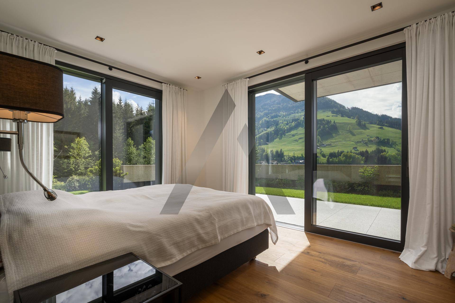 Schlafzimmer mit Holzboden und großen Fenstern, die einen direkten Zugang zum Garten bieten.