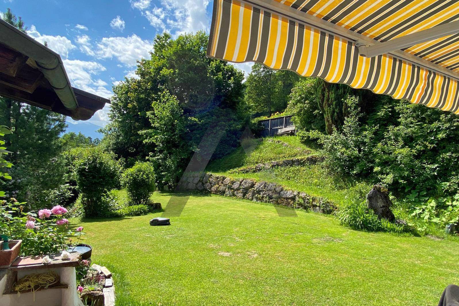 Grüner Garten mit Rasenfläche und Blumen unter einer gestreiften Markise.