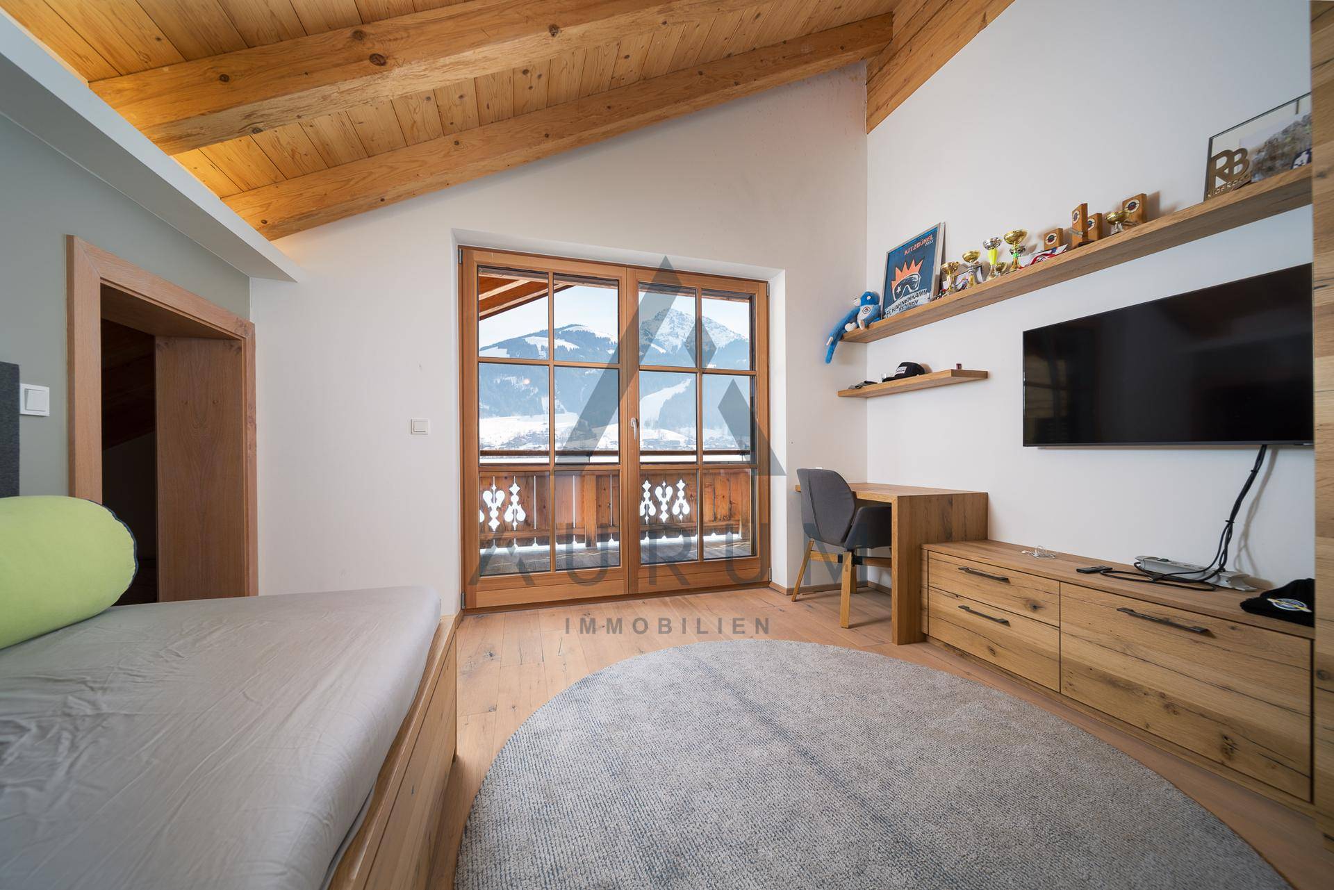 Kinderzimmer mit Holzbalkendecke, Schreibtisch und Zugang zum Balkon mit Bergblick.