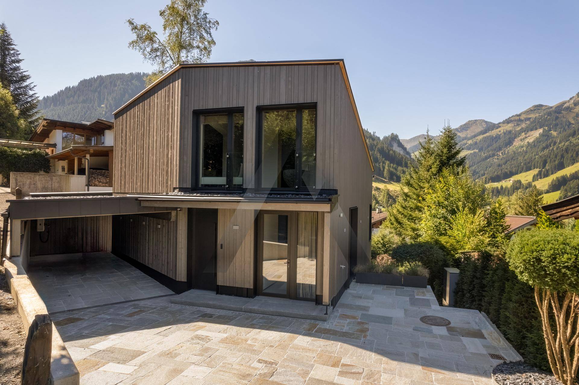 Moderne Villa mit Carport, gepflastertem Vorplatz und Bergblick in alpiner Umgebung.