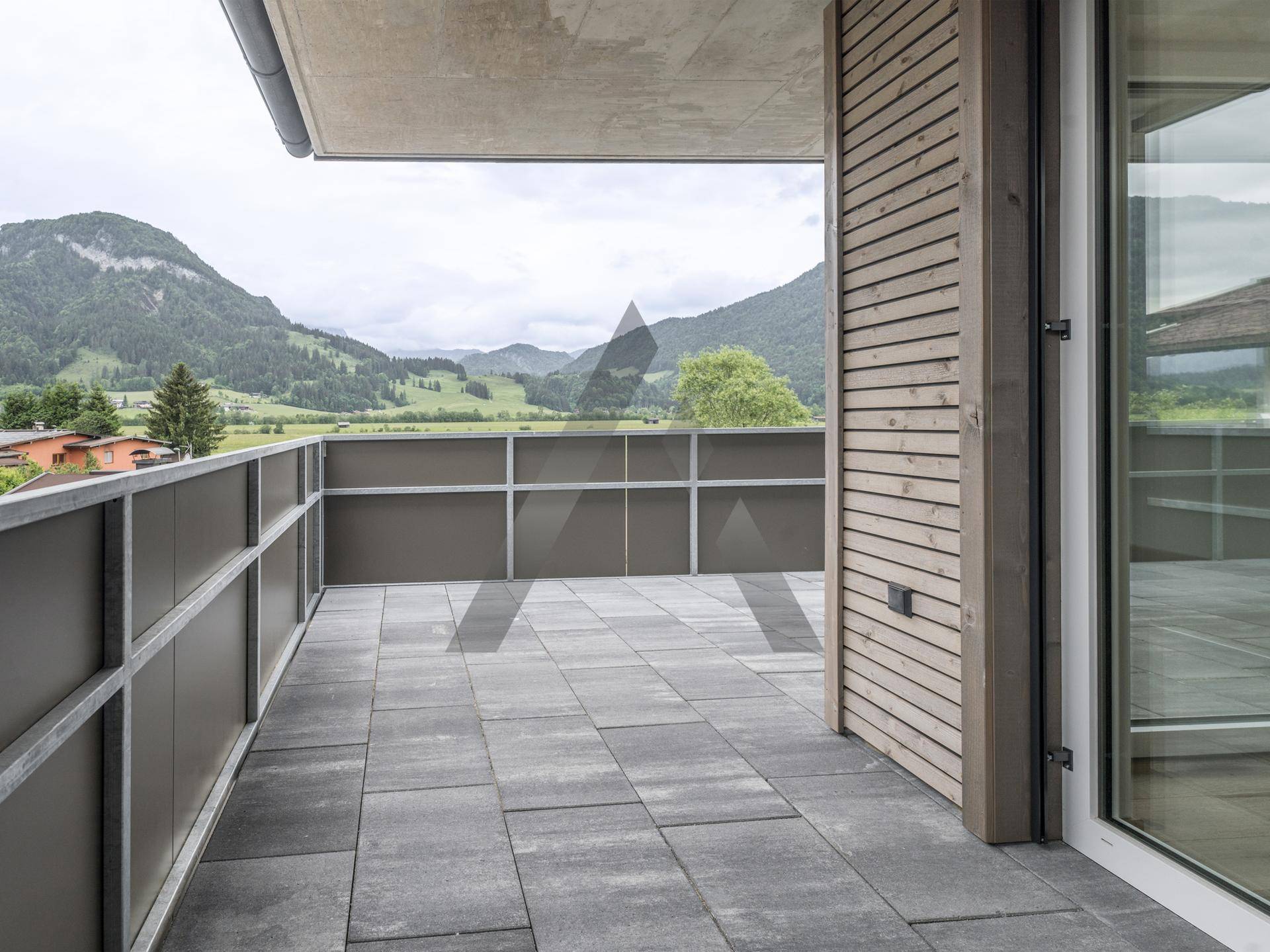 Geräumiger Balkon mit Fliesenboden und modernem Geländer, bietet einen schönen Blick auf die umliegende Berglandschaft.