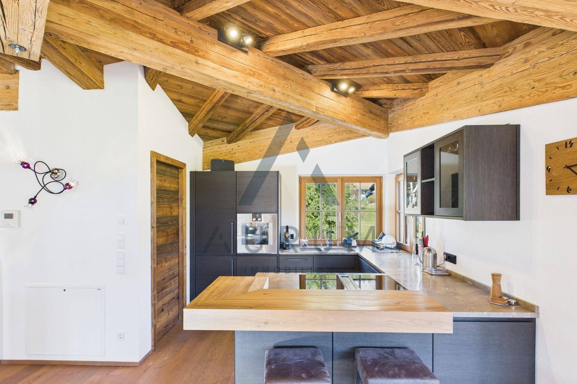 Moderne Küche mit dunklen Schränken, Holztheke und integrierten Geräten unter Holzbalkendecke.