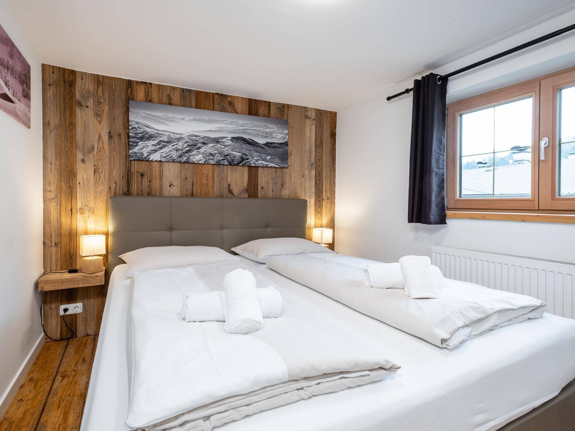 Schlafzimmer mit zwei Einzelbetten, Holzwandverkleidung und Dielenboden, Blick auf verschneite Landschaft.