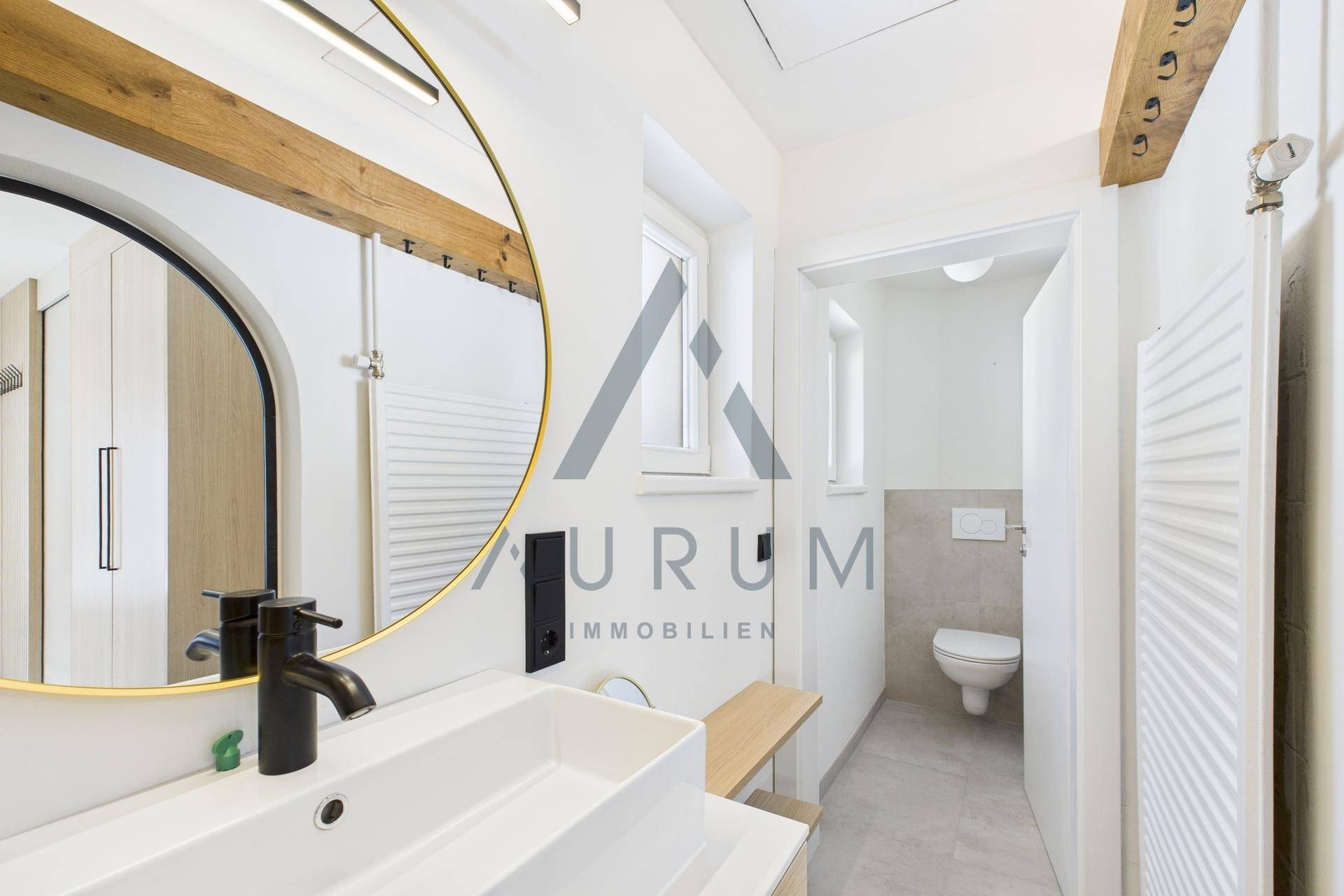 Modernes Badezimmer mit stilvollem Spiegel, Waschtisch und separatem WC-Bereich.