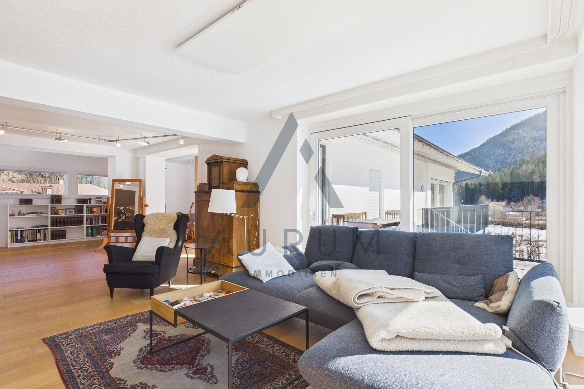 Gemütliches Wohnzimmer mit Sofa, Teppich und Zugang zu einem Balkon mit Bergblick.