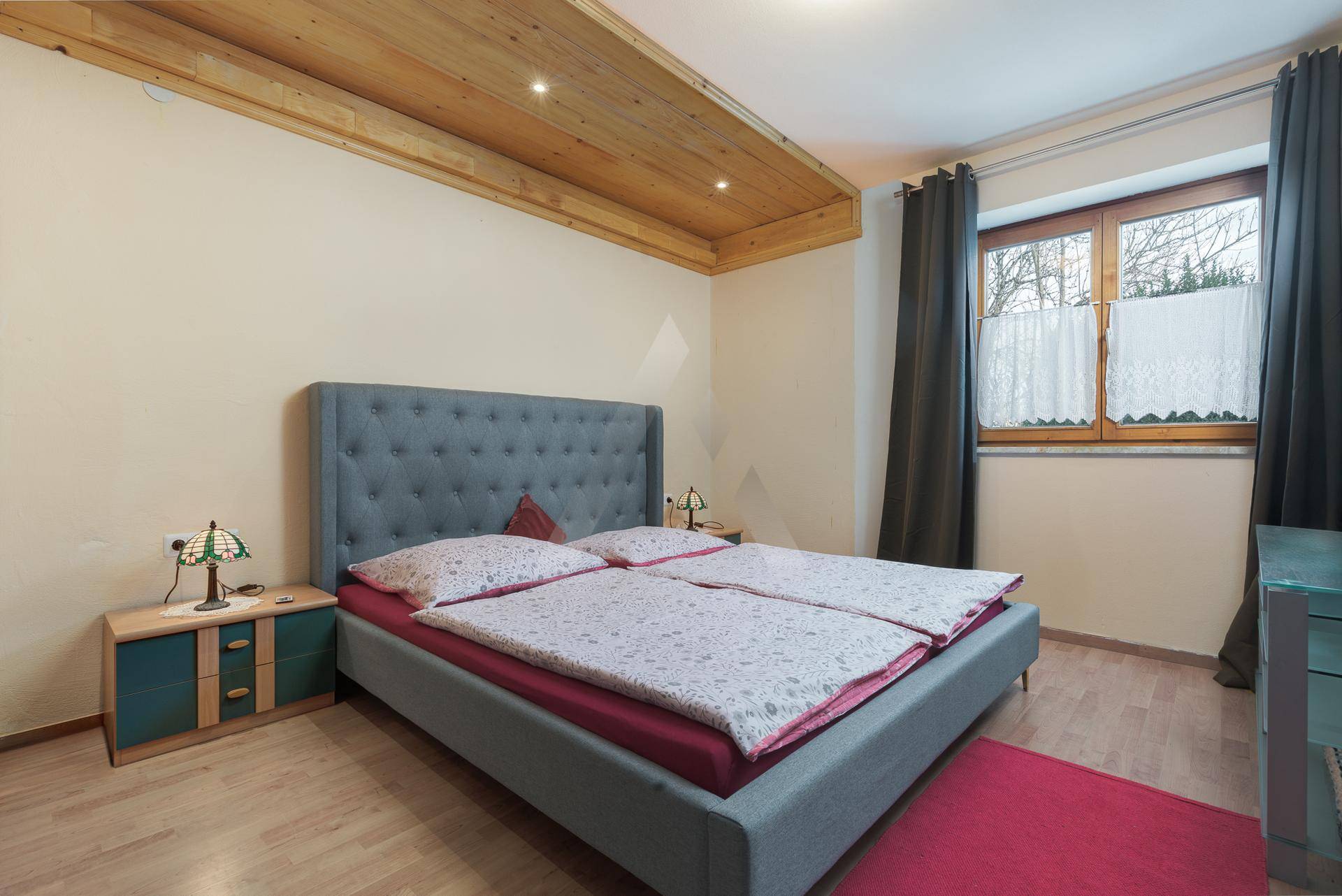 Helles Schlafzimmer mit Doppelbett, Holzdecke und Parkettboden, durchflutet von Tageslicht.