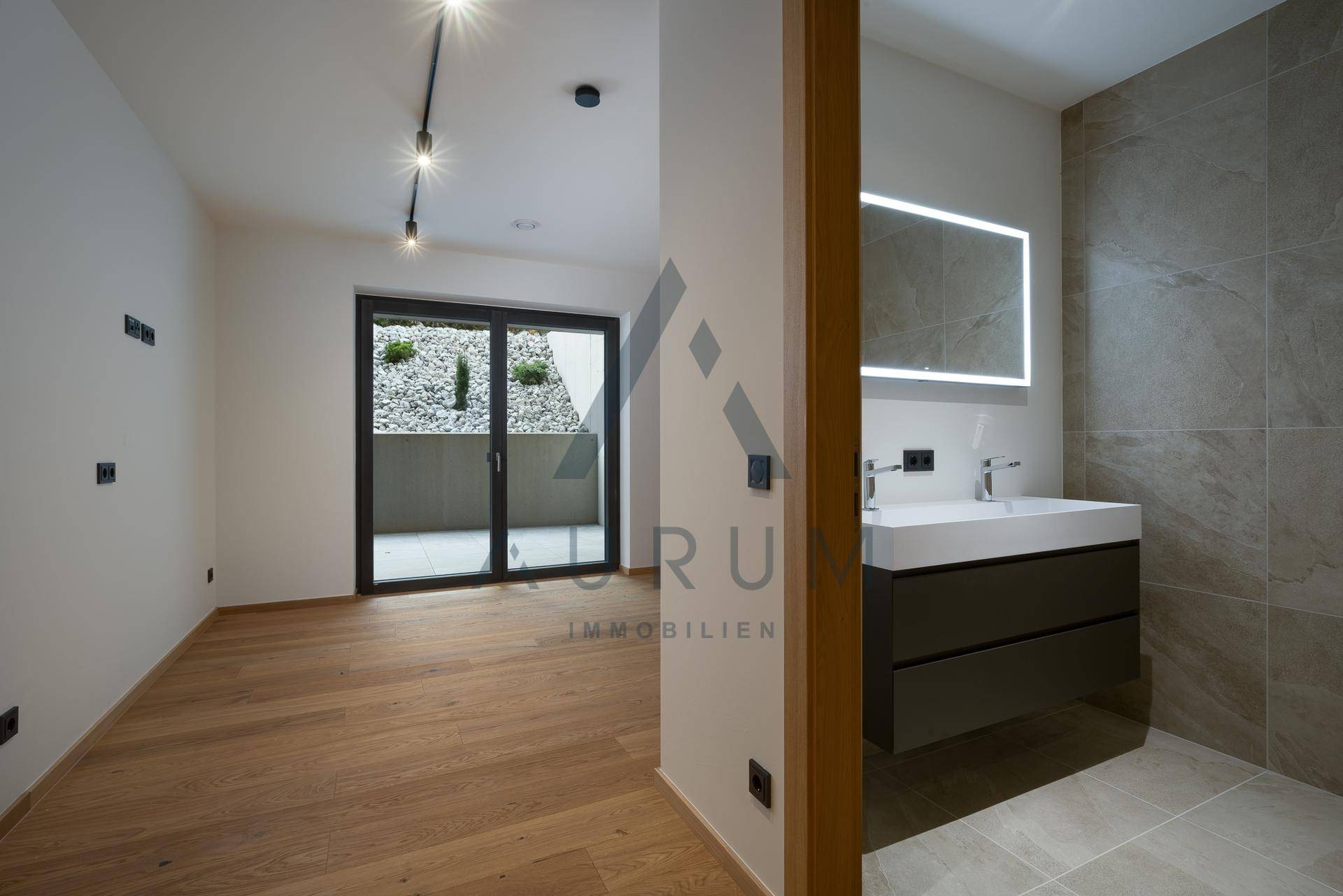 Heller Raum mit Holzboden und angrenzendem modernen Badezimmer mit Waschtisch.