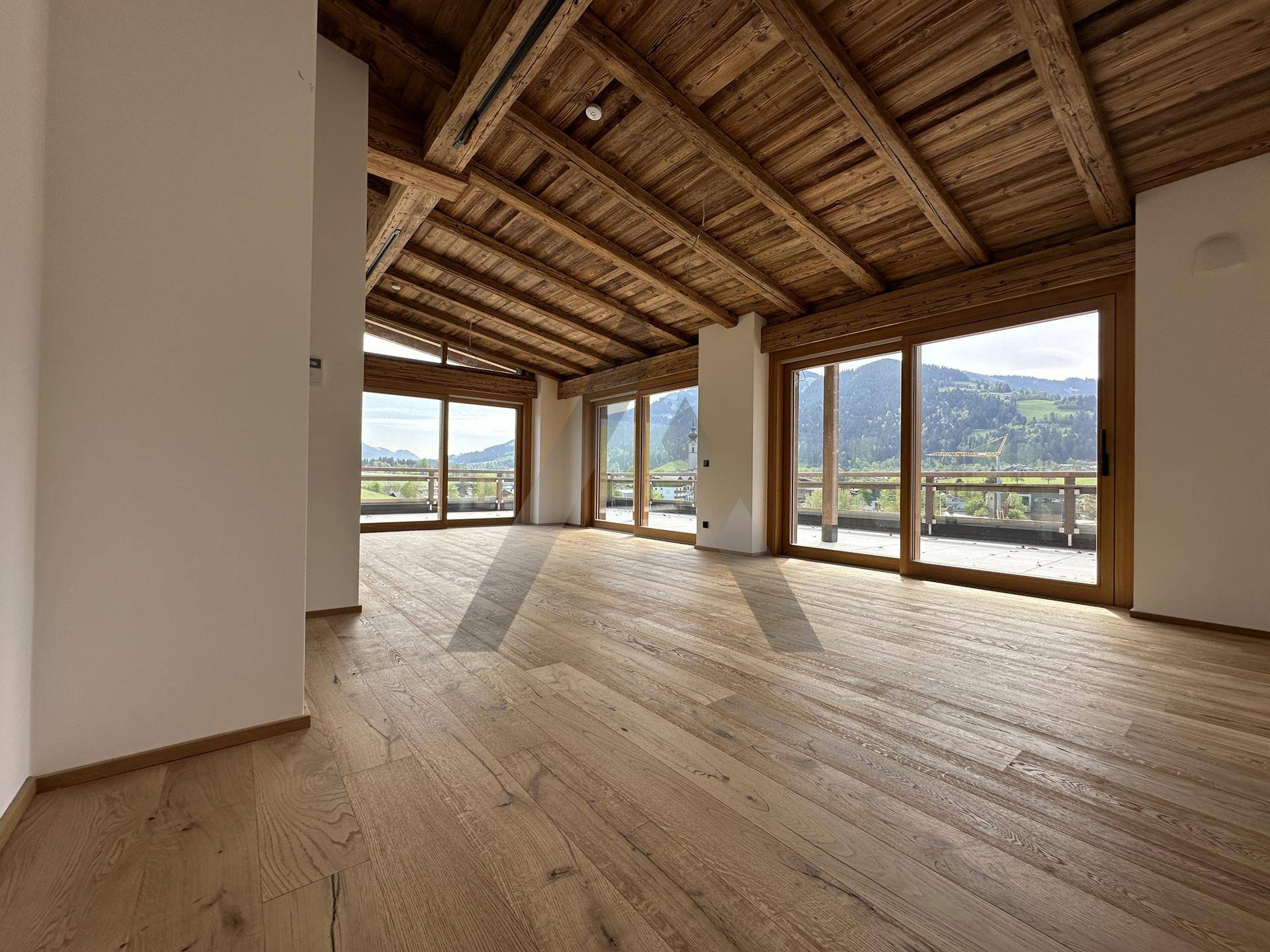 Heller Wohnbereich mit rustikaler Holzbalkendecke und weitem Blick auf die umliegende Berglandschaft.