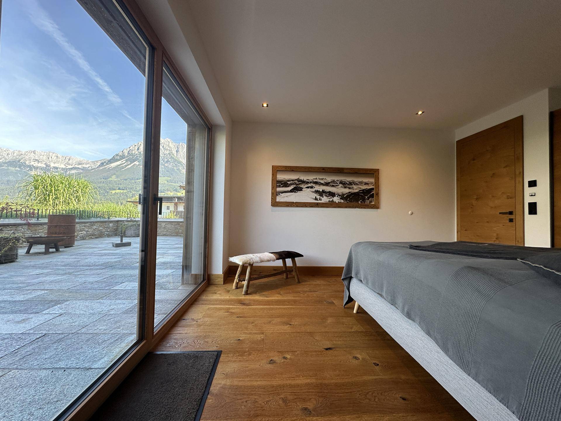 Geräumiges Schlafzimmer mit Holzboden, großen Fenstern und direktem Terrassenzugang mit Bergblick.